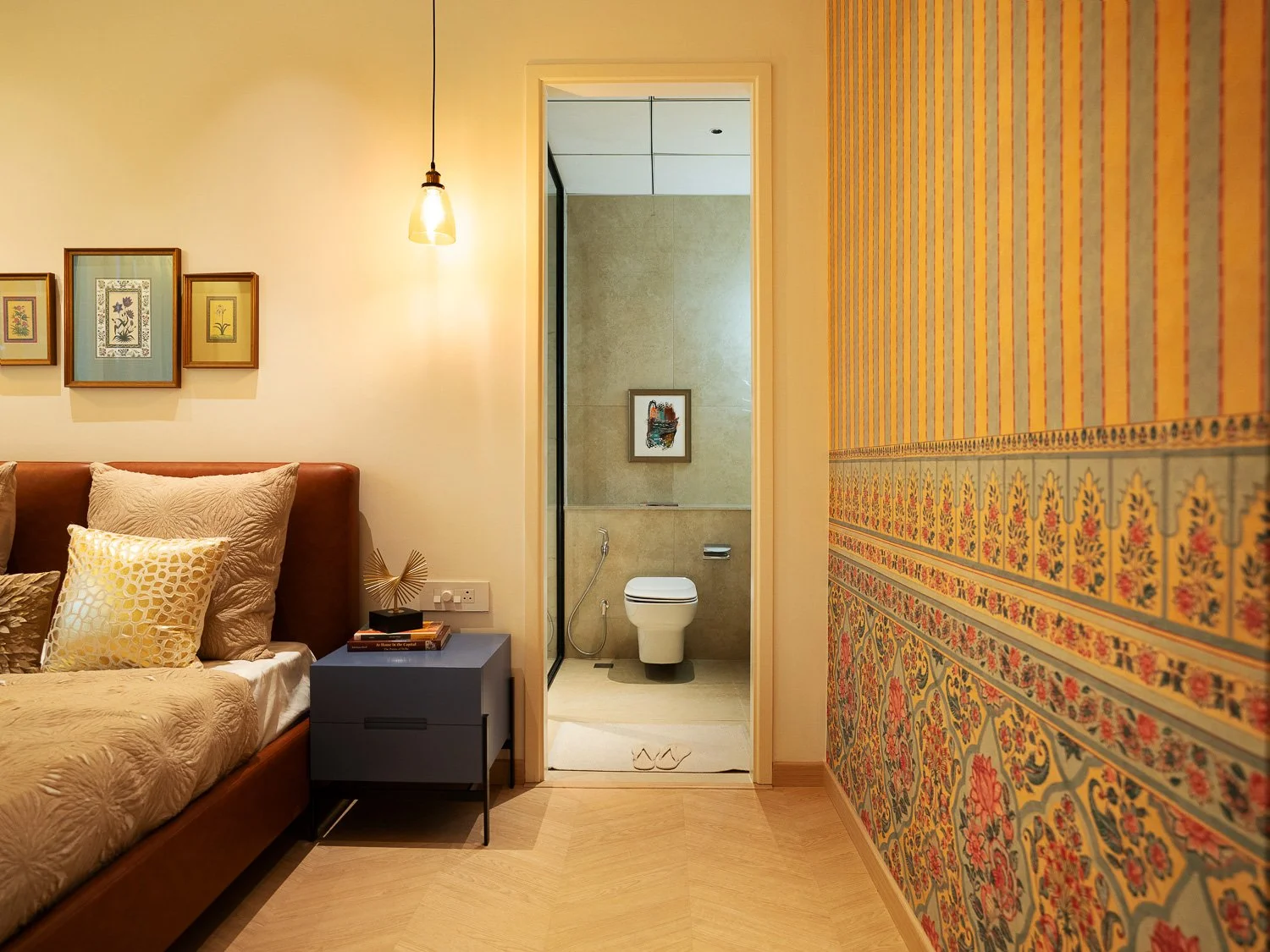 A bedroom with a bed, pillows, a nightstand, and a bathroom with a toilet visible through an open doorway.