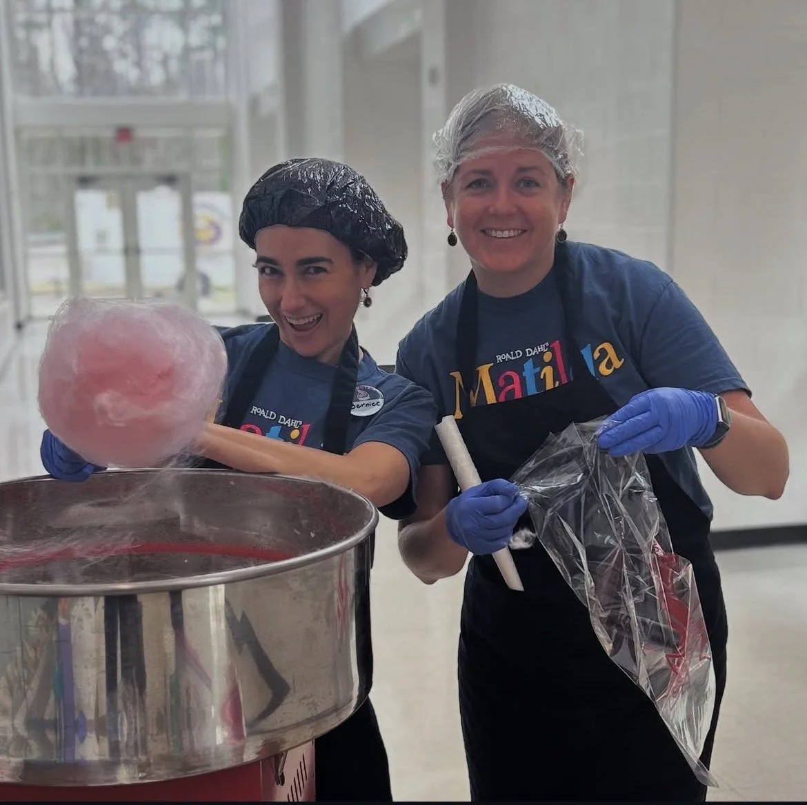 Two women wearing hairnets and gloves making cotton candy in a bright, indoor setting.