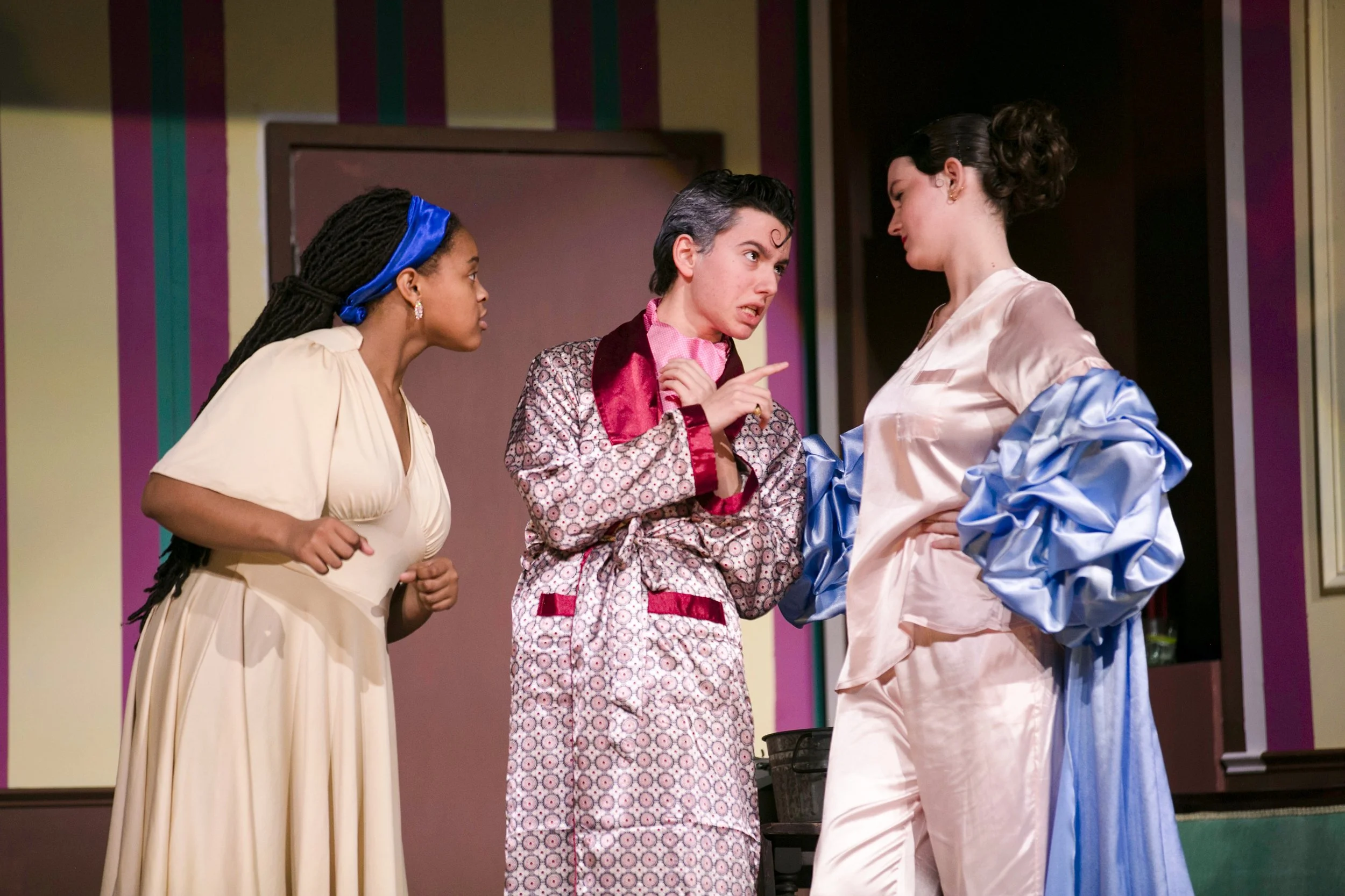 Three women in colorful pajamas having a heated discussion on stage during a theater performance.