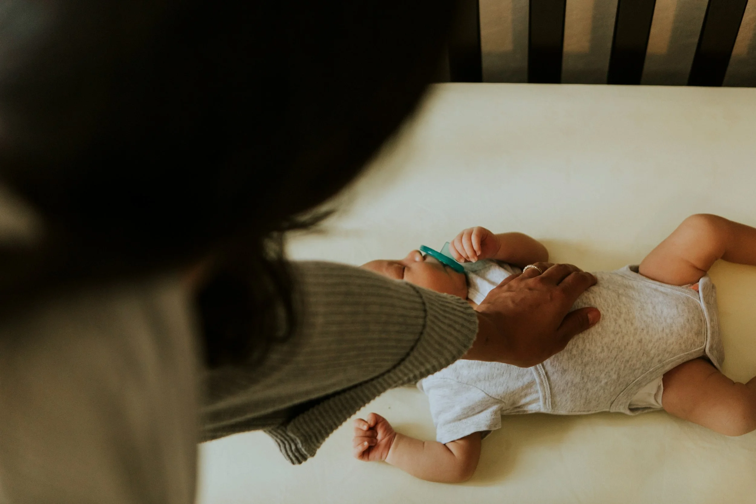 Person lying on a changing table with a pacifier in baby's mouth, holding the baby’s head and touching the baby's chest.