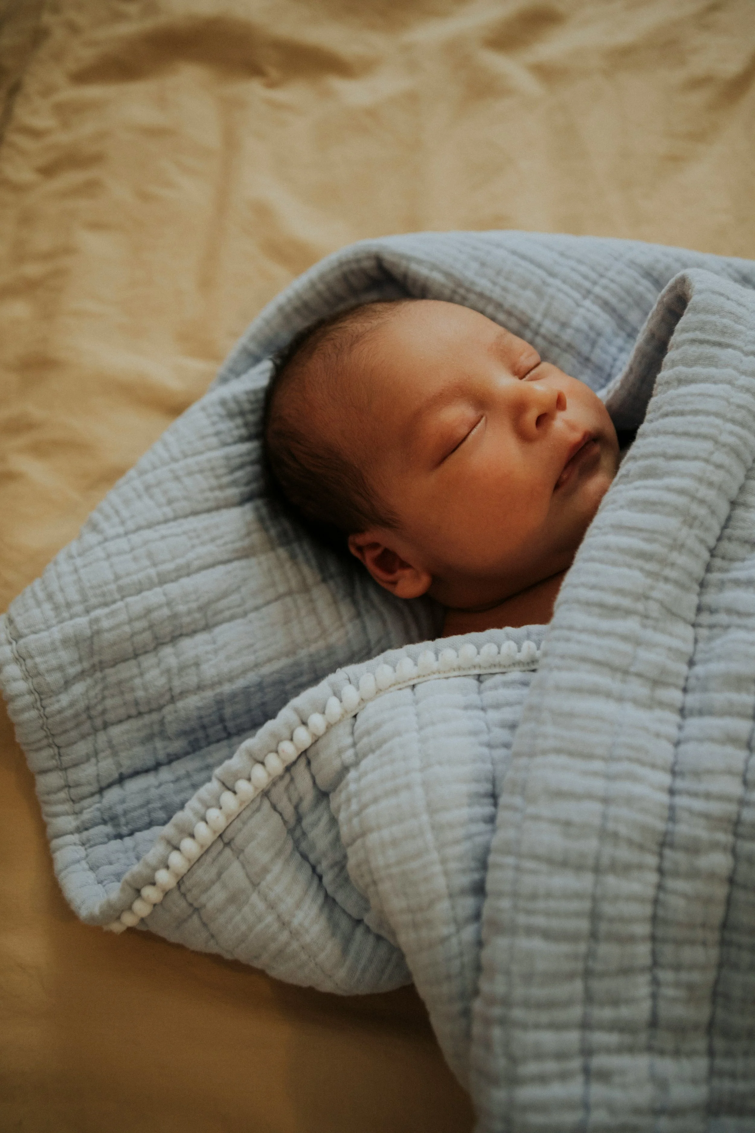 A peacefully sleeping baby wrapped in a light, checkered blanket.