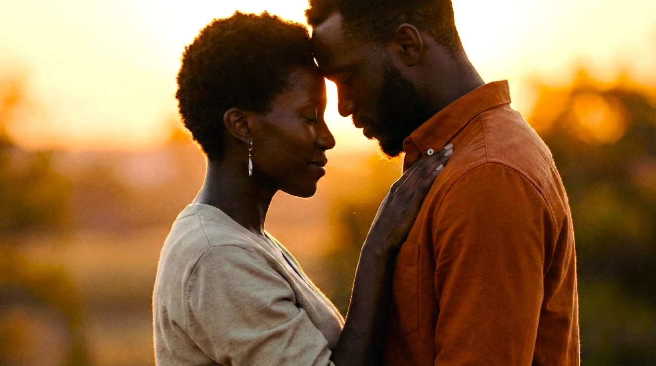 A couple standing close with foreheads and noses touching during sunset, eyes closed, in an outdoor setting.
