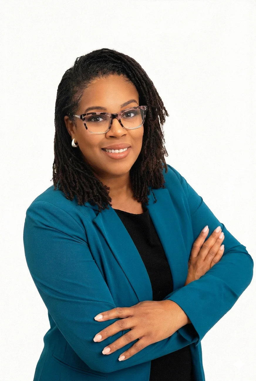 Professional woman with glasses, wearing a teal blazer, crossing her arms, smiling, against a plain white background.