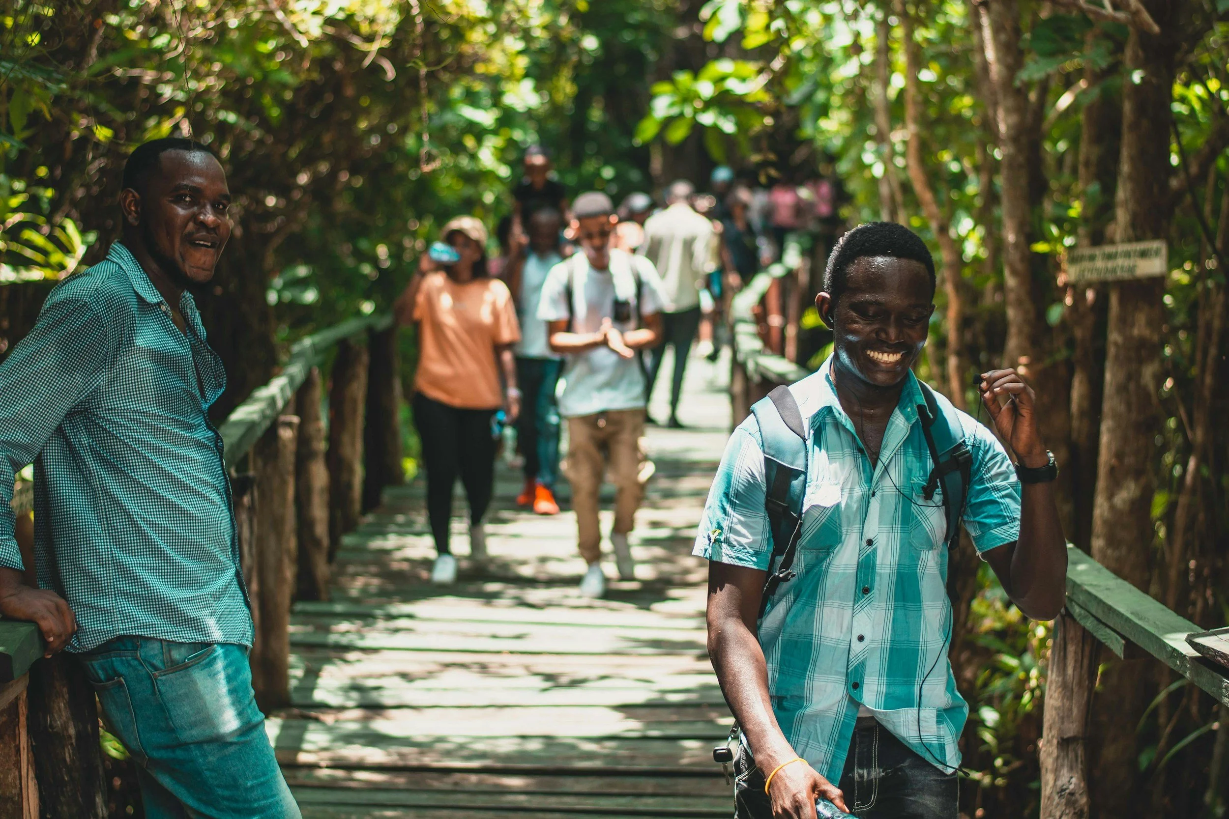 Group of people walking on a wooden bridge in a lush green forest, smiling and enjoying their hike.