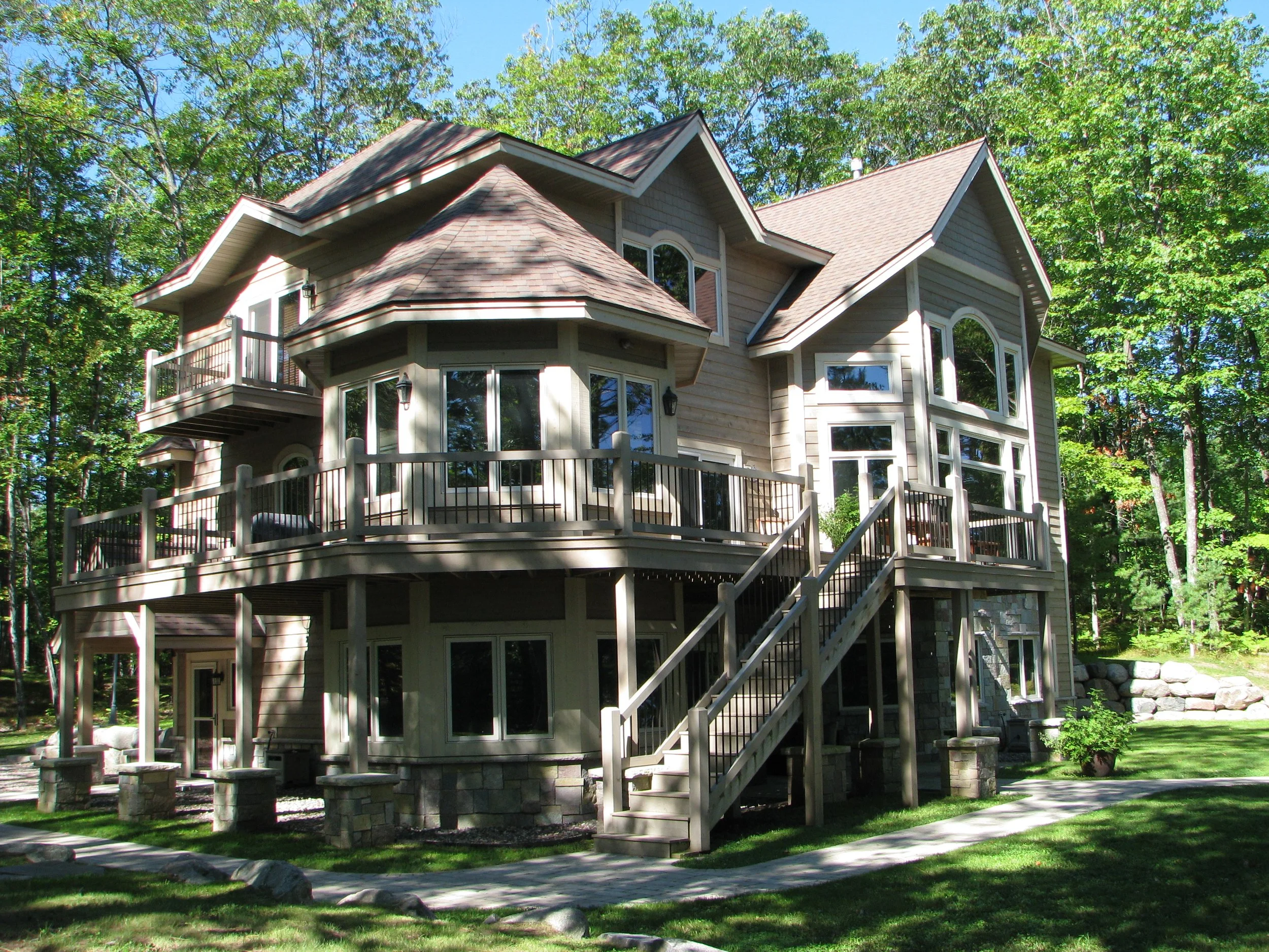 Multi-story house with multiple decks and large windows surrounded by trees and a well-maintained lawn.
