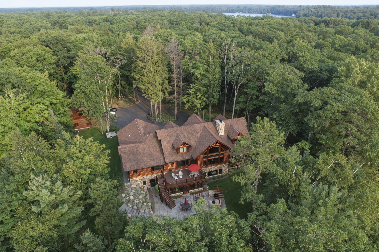 A large house surrounded by dense green trees with a deck, patio, and outdoor seating area.