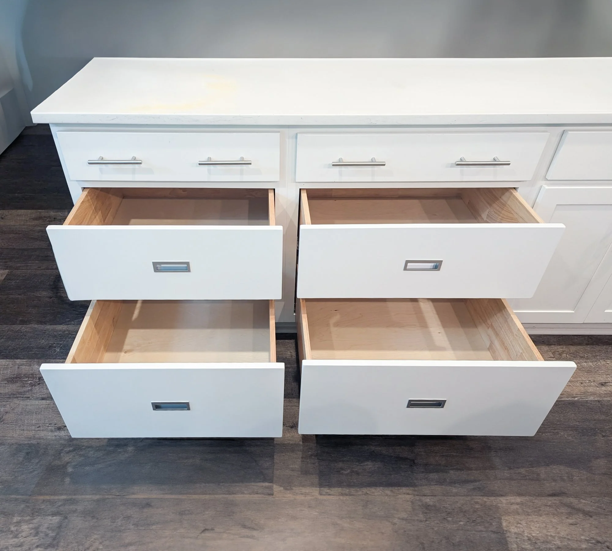 Open white kitchen drawers with empty wooden interiors, set on dark wood flooring.
