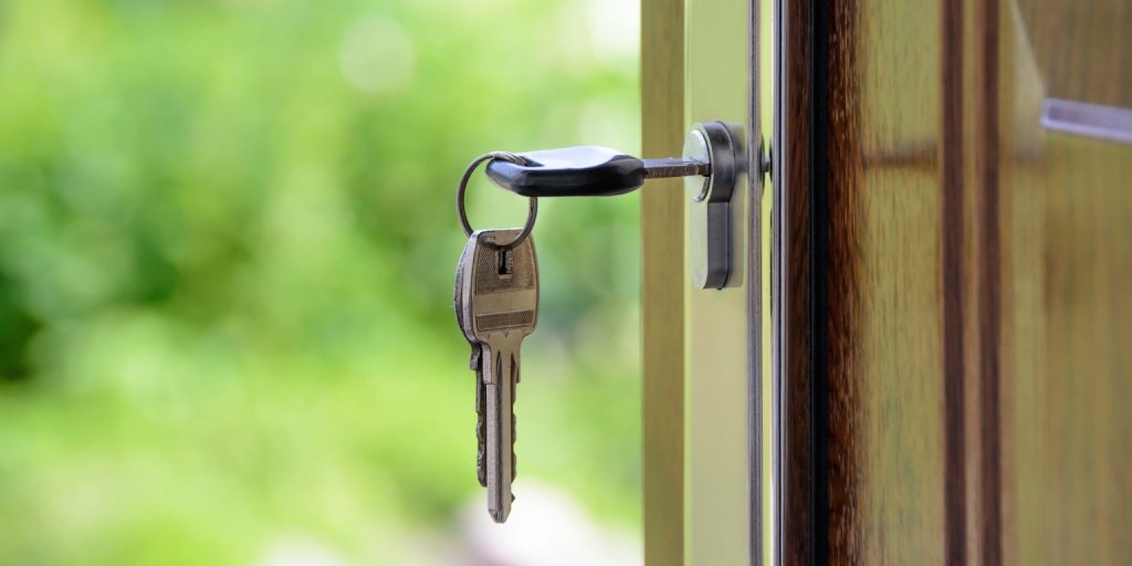 Close-up of a key inserted into a door lock, with a blurred green outdoor background.