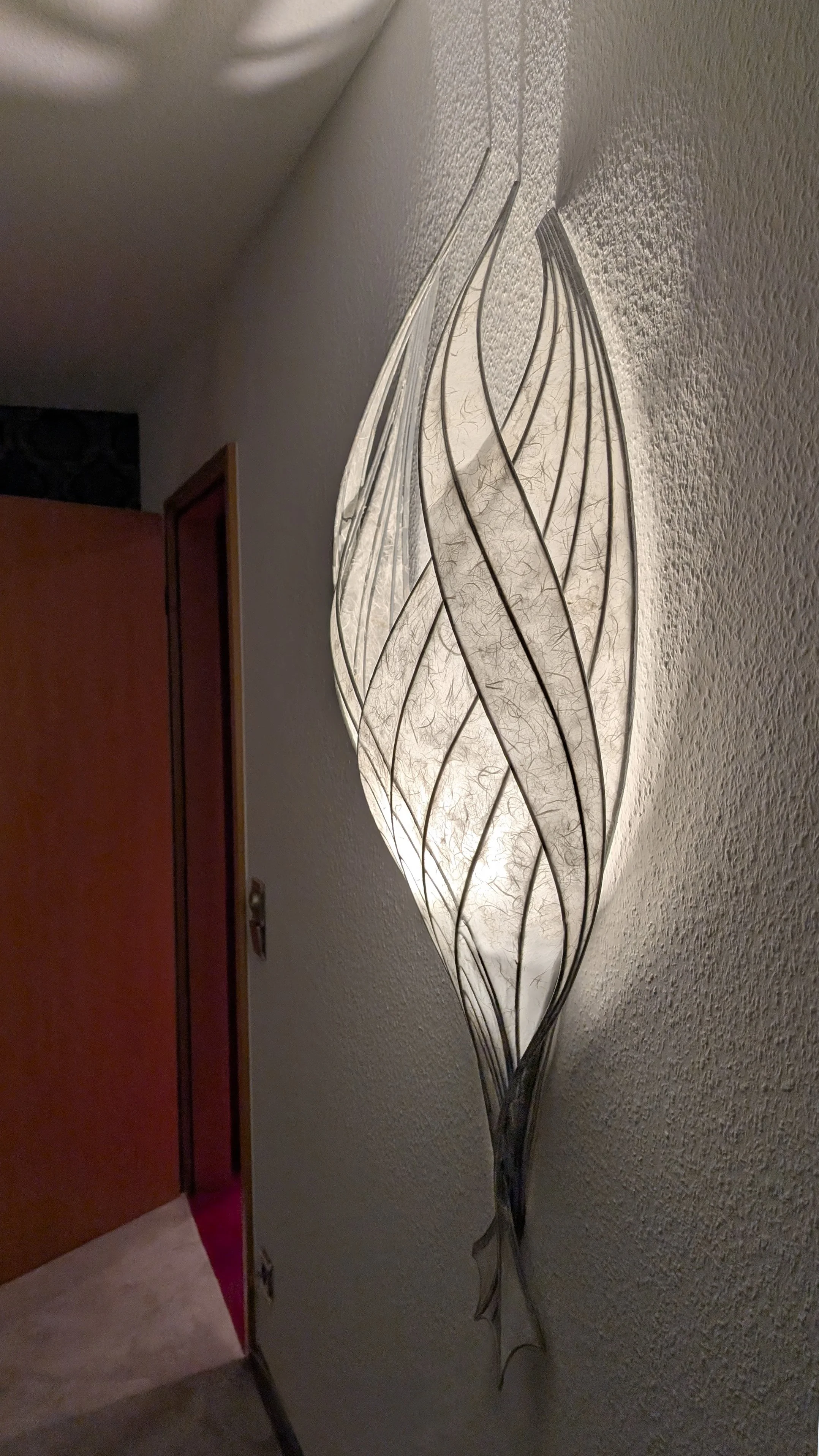 Wandleuchte mit dünnen, geschwungenem Peddigrohr und weißen, elastischen Schmetterlingsflügeln, die das Licht warm abgeben.