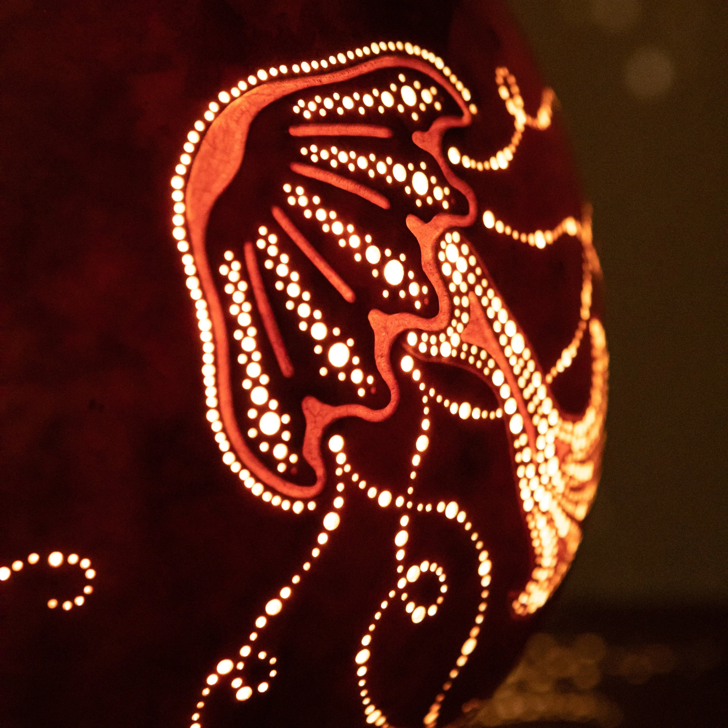 Ein beleuchteter Kürbis mit einem geschnitzten Totenkopf-Design und Mustern in warmem Orange.