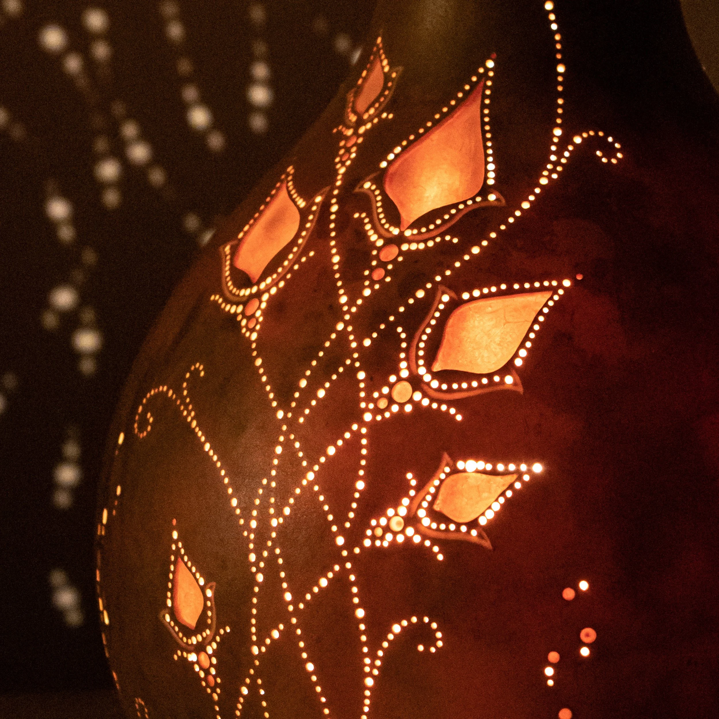 Eine Laterne mit stilisiertem Blättermuster, durch das Licht scheint und Schatten wirft.