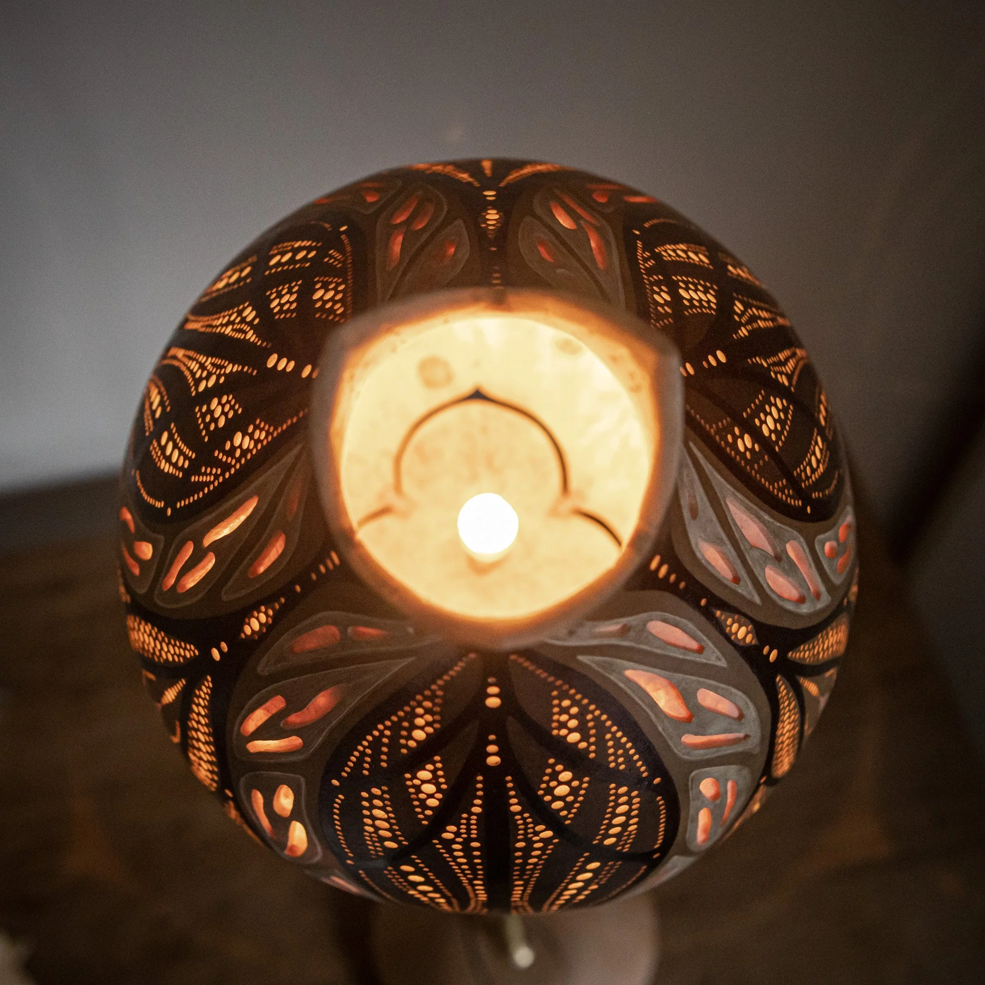 Deckenleuchte mit filigranem, geschnitztem Muster, das Licht strahlt durch die Aussparungen, erzeugt warme Atmosphäre.