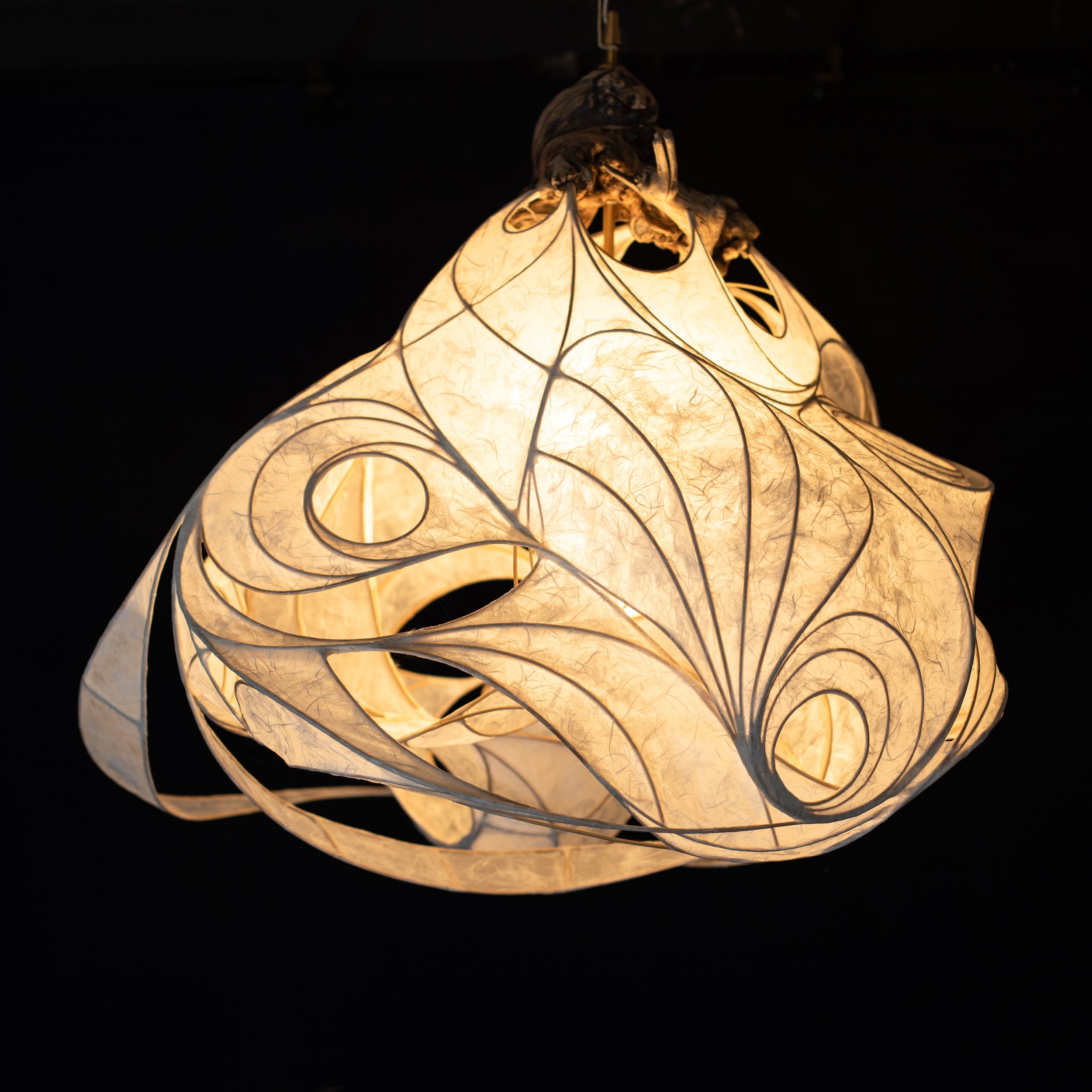 Eine moderne, kreative Deckenlampe aus Papier mit schwarz umrandeten, geschwungenen Mustern, die warmes Licht ausstrahlt.