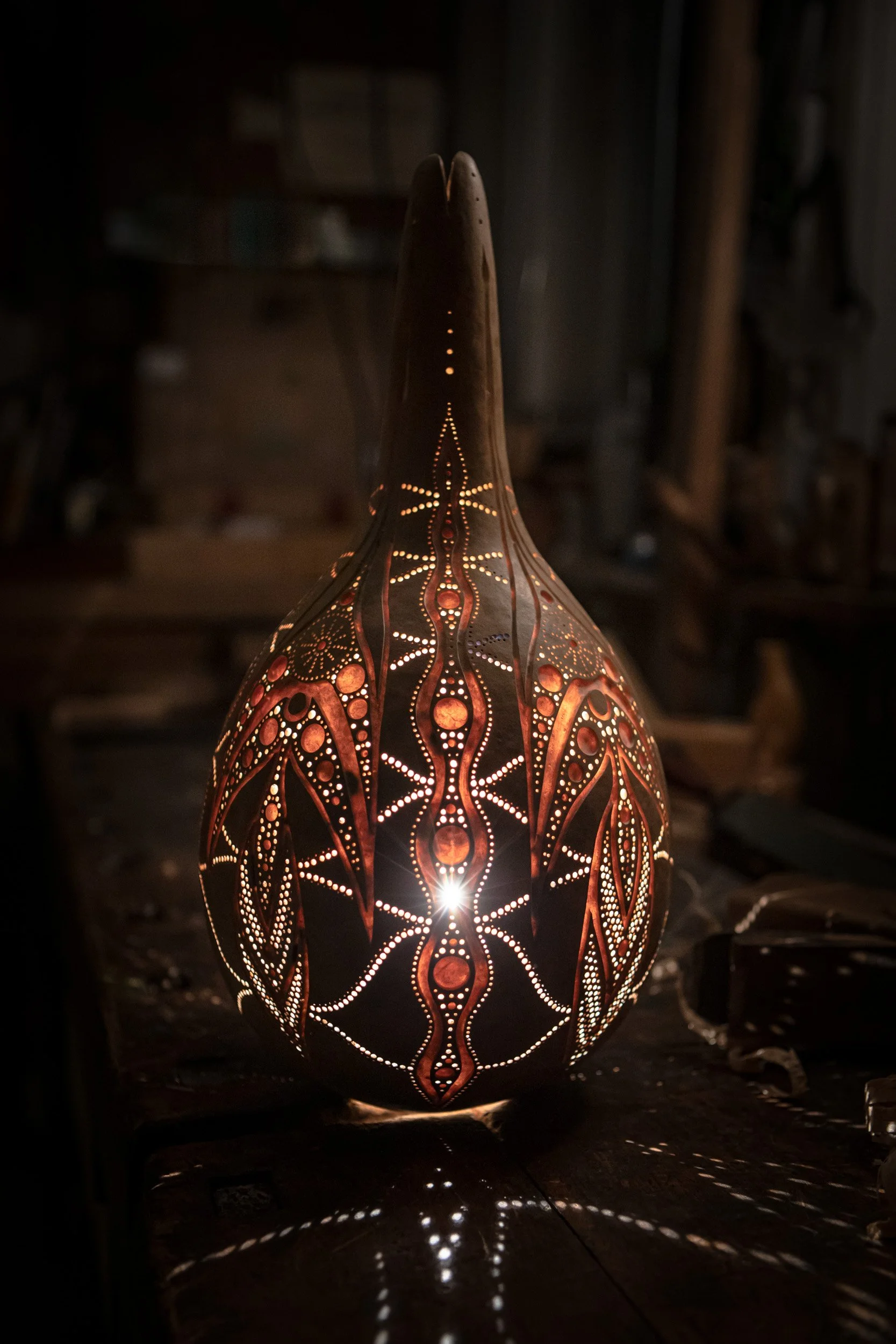 Oberes Ende einer ornamentalen, ausgehöhlten Keramiklampe mit perforierten Mustern, die Licht durchscheinen lassen, auf einem dunklen Tisch in einem Workshopraum.