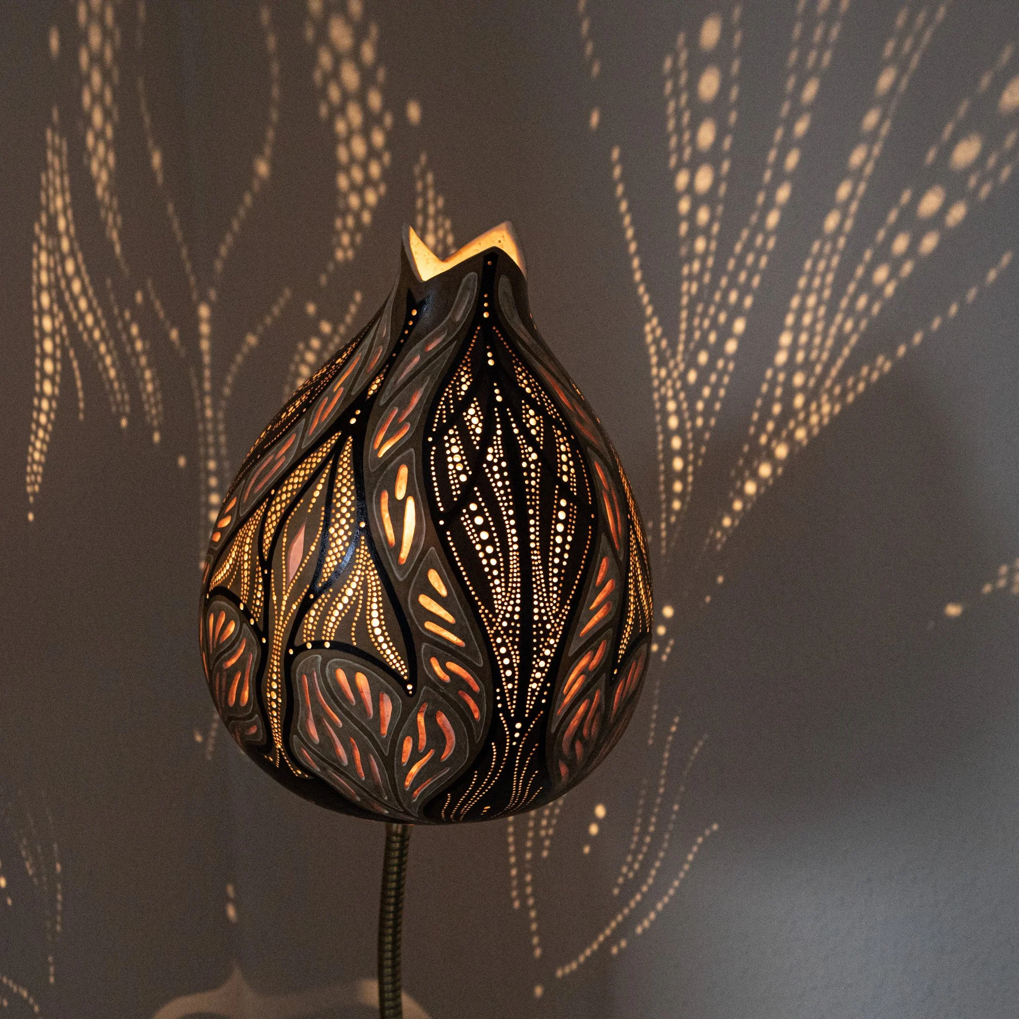 Ein dekorativer Lampenschirm aus Metall mit filigranen Mustern, der warmes Licht abstrahlt und Schatten an die Wand wirft.