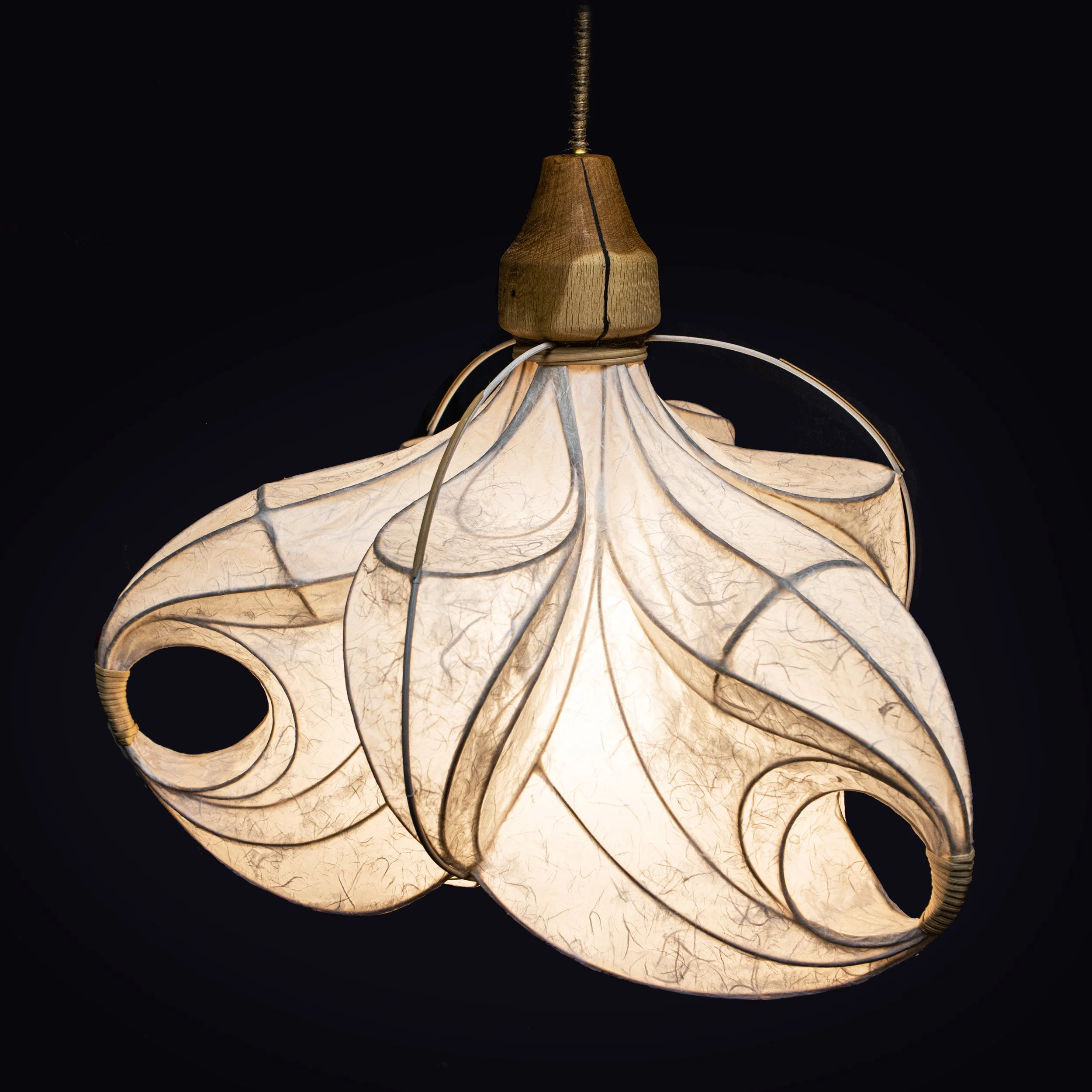 Hängelampe mit Blattmuster aus Papier und Holz, leuchtend gegen dunklen Hintergrund.