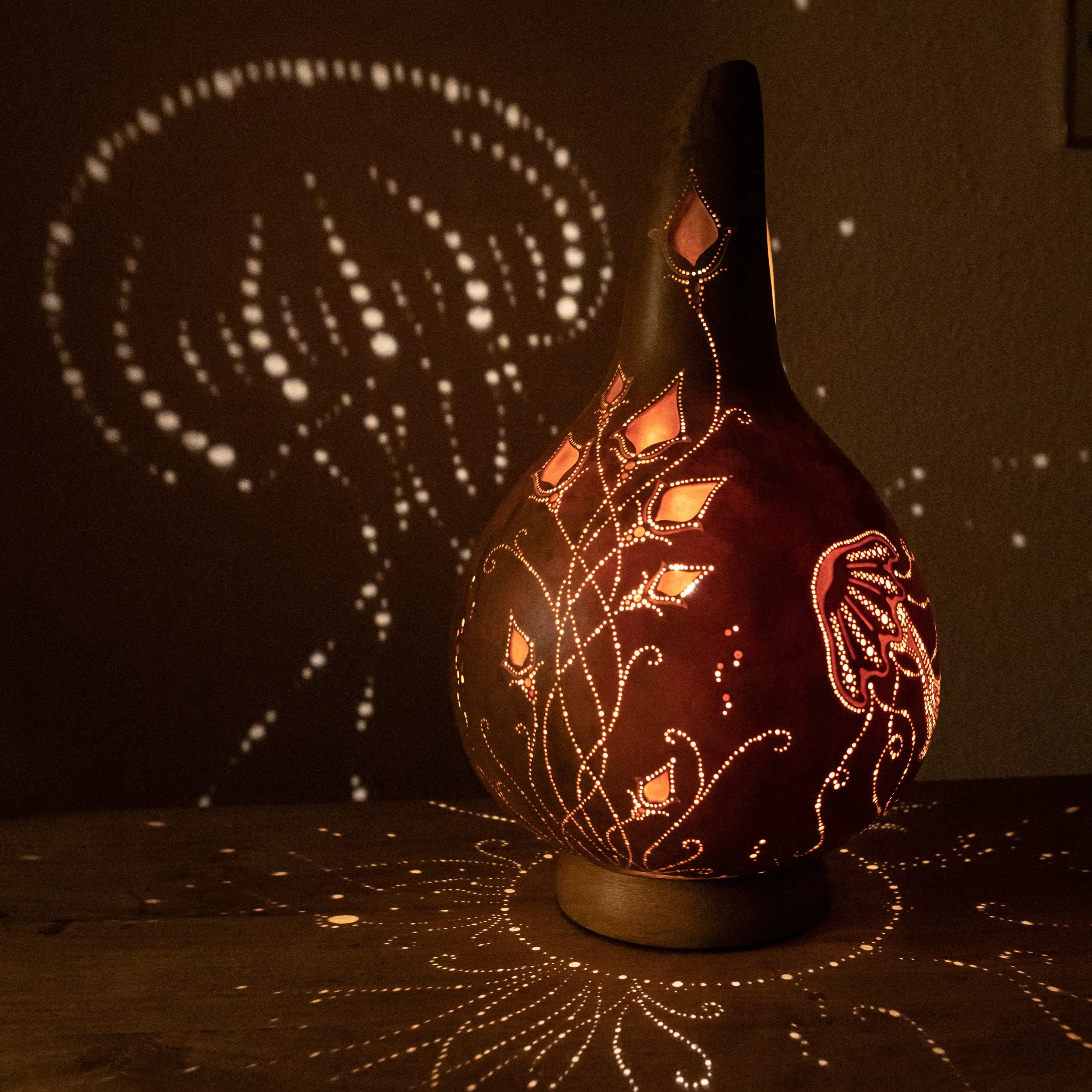 Eine dekorative, leuchtende Vase mit Muster, das Licht durch kleine Löcher strahlen lässt und Schatten an die Wand wirft.