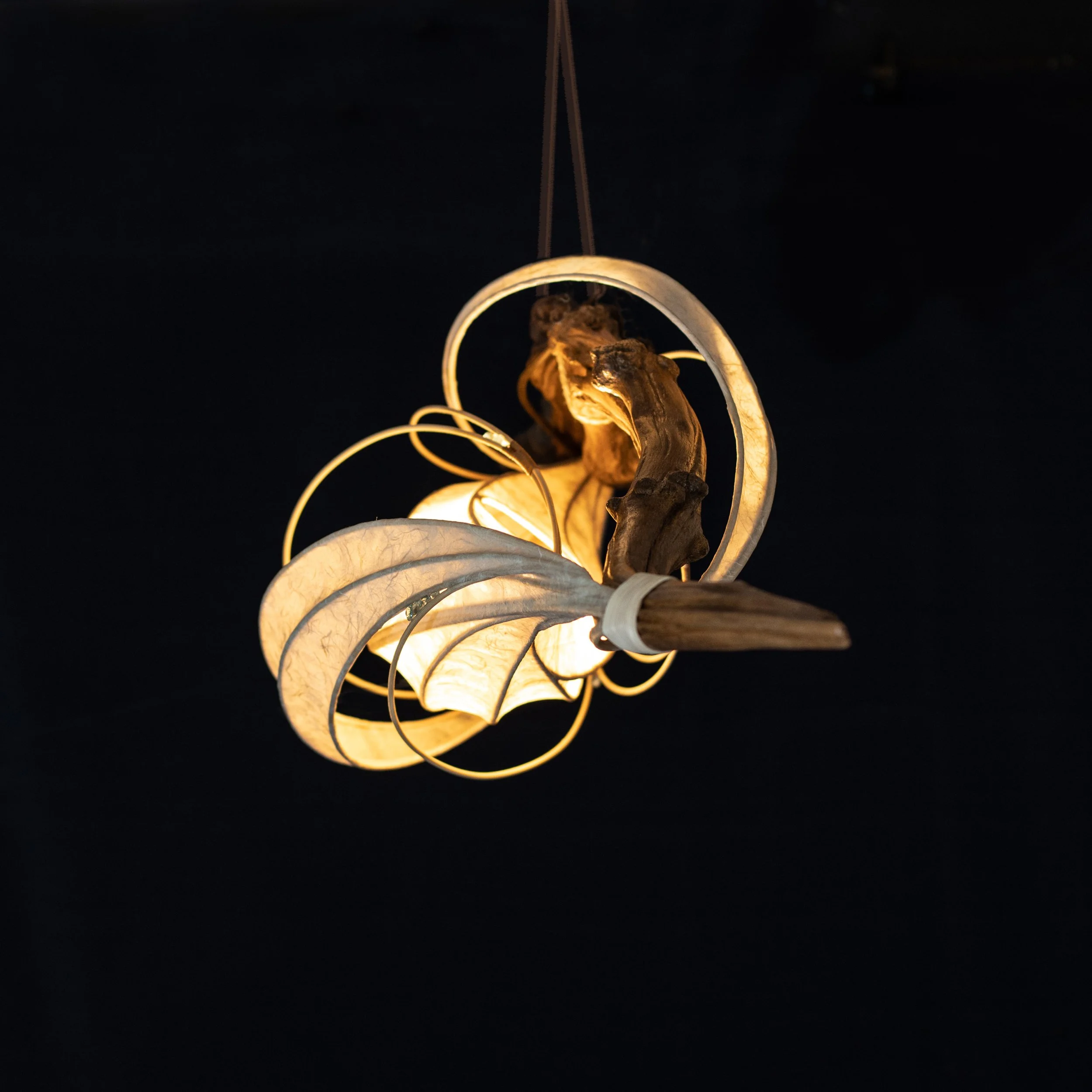 Hängelampe mit einem kunstvollen Design, kombiniert aus Holz und Papier, leuchtet vor dunklem Hintergrund.