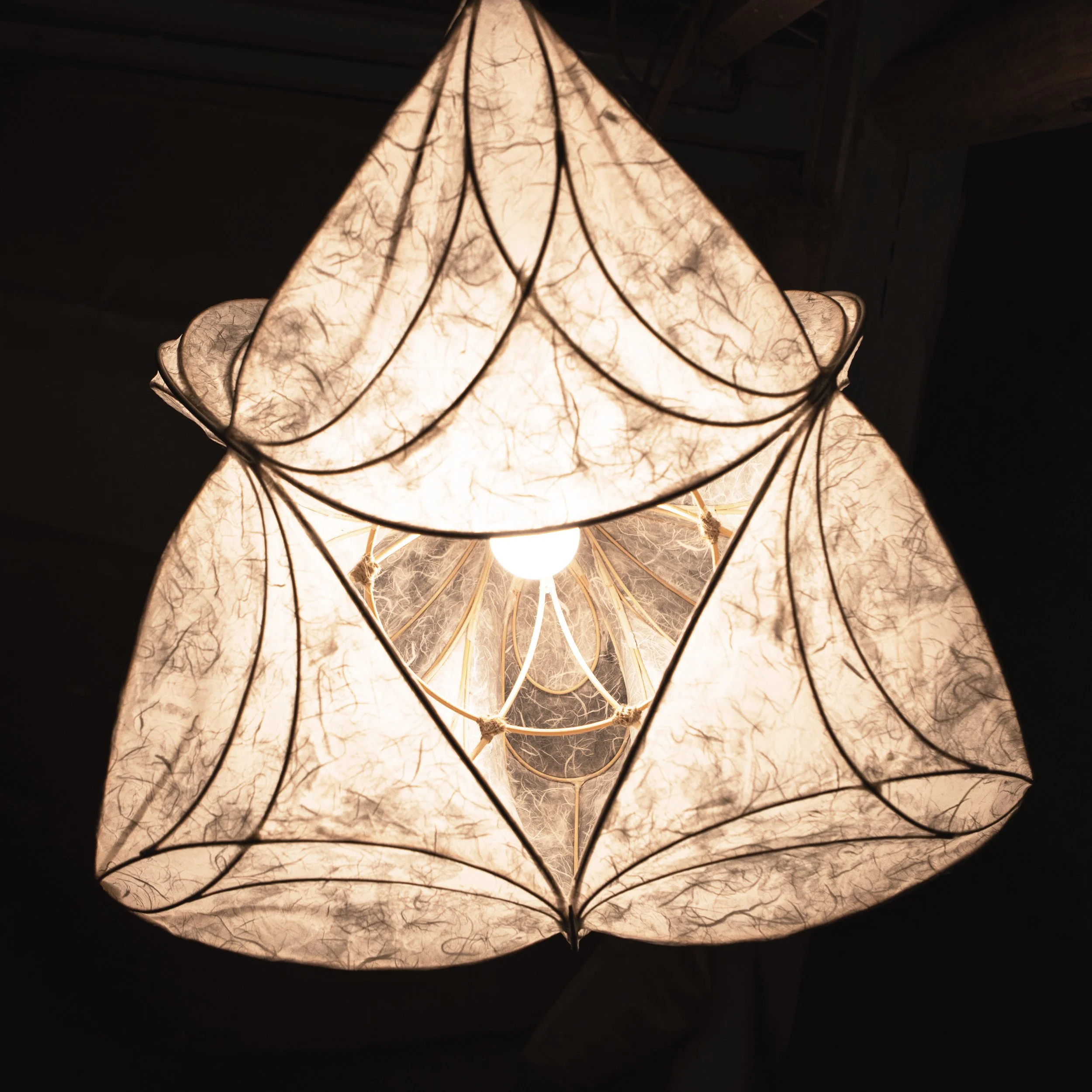 Hängelampe mit sechs Stofflampenschirmen, die einen warmen Lichtschein abgeben, im Dunkeln.