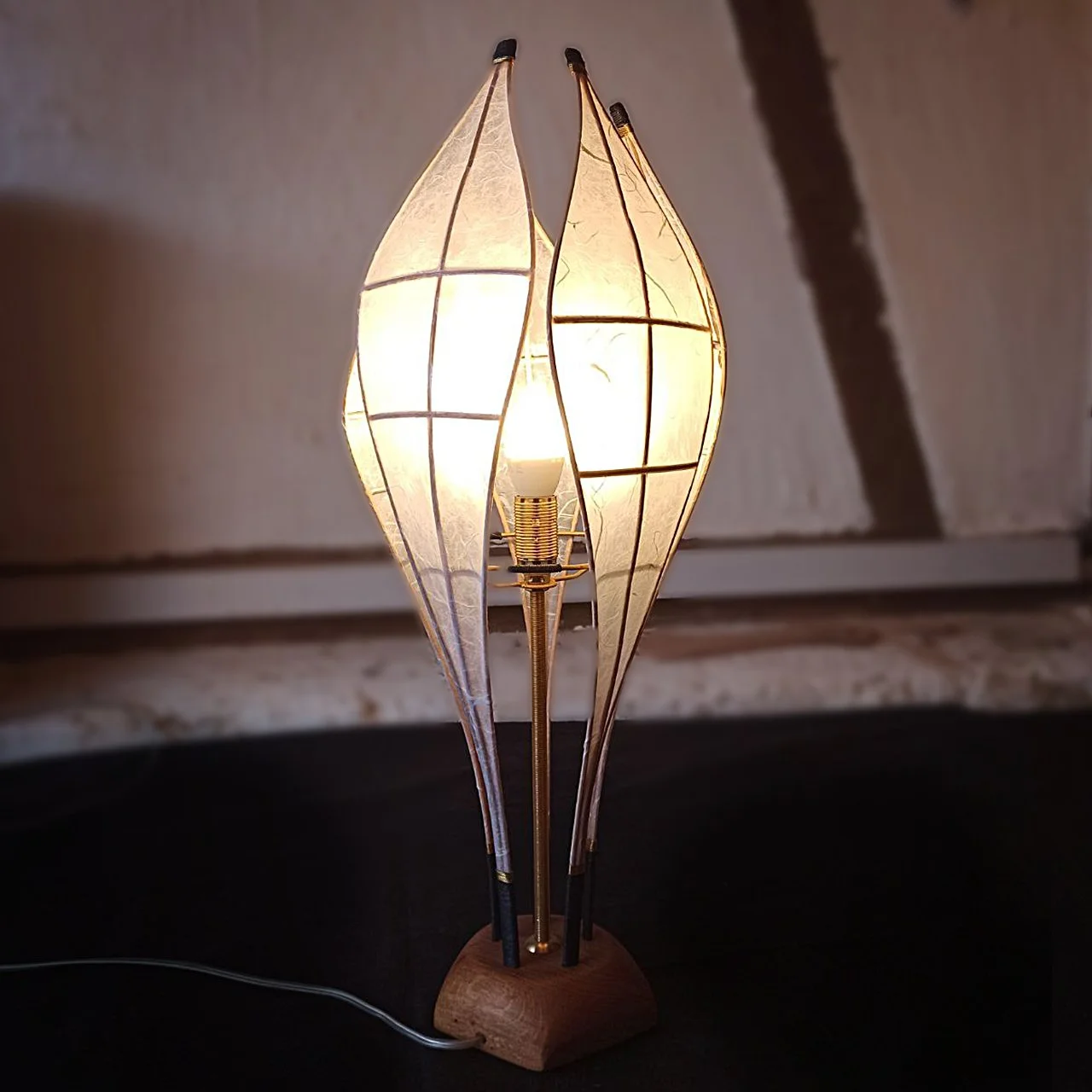 Eine stilvolle Tischlampe mit einem Holzsockel und einem glas- oder kunststoffgefassten Lampenschirm, der an der Seite offen ist, das Licht lässt den Schirm hell erstrahlen.