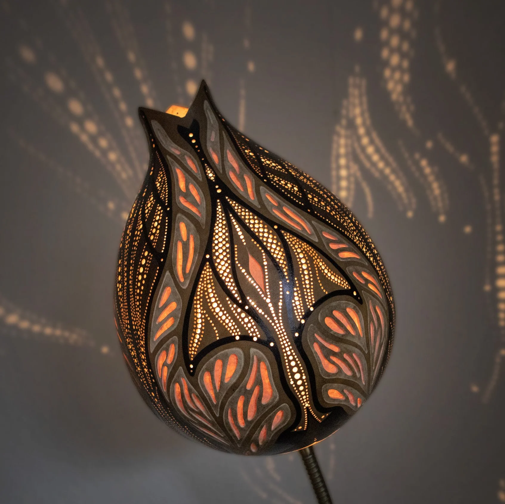 Eine dekorative Leuchte mit filigranem, pflanzenähnlichem Muster, das warm orange Licht ausstrahlt und Schatten an die Wand wirft.