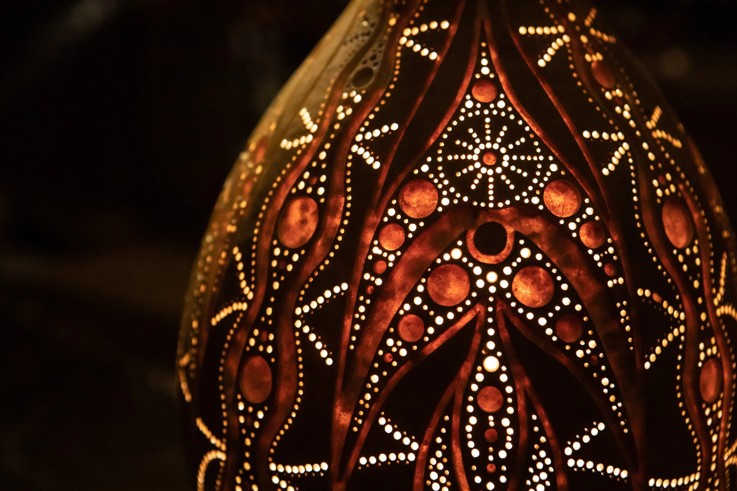 Verzierter, leuchtender Lampenschirm mit filigranen Mustern und kleinen Löchern, die warmes Licht ausstrahlen.