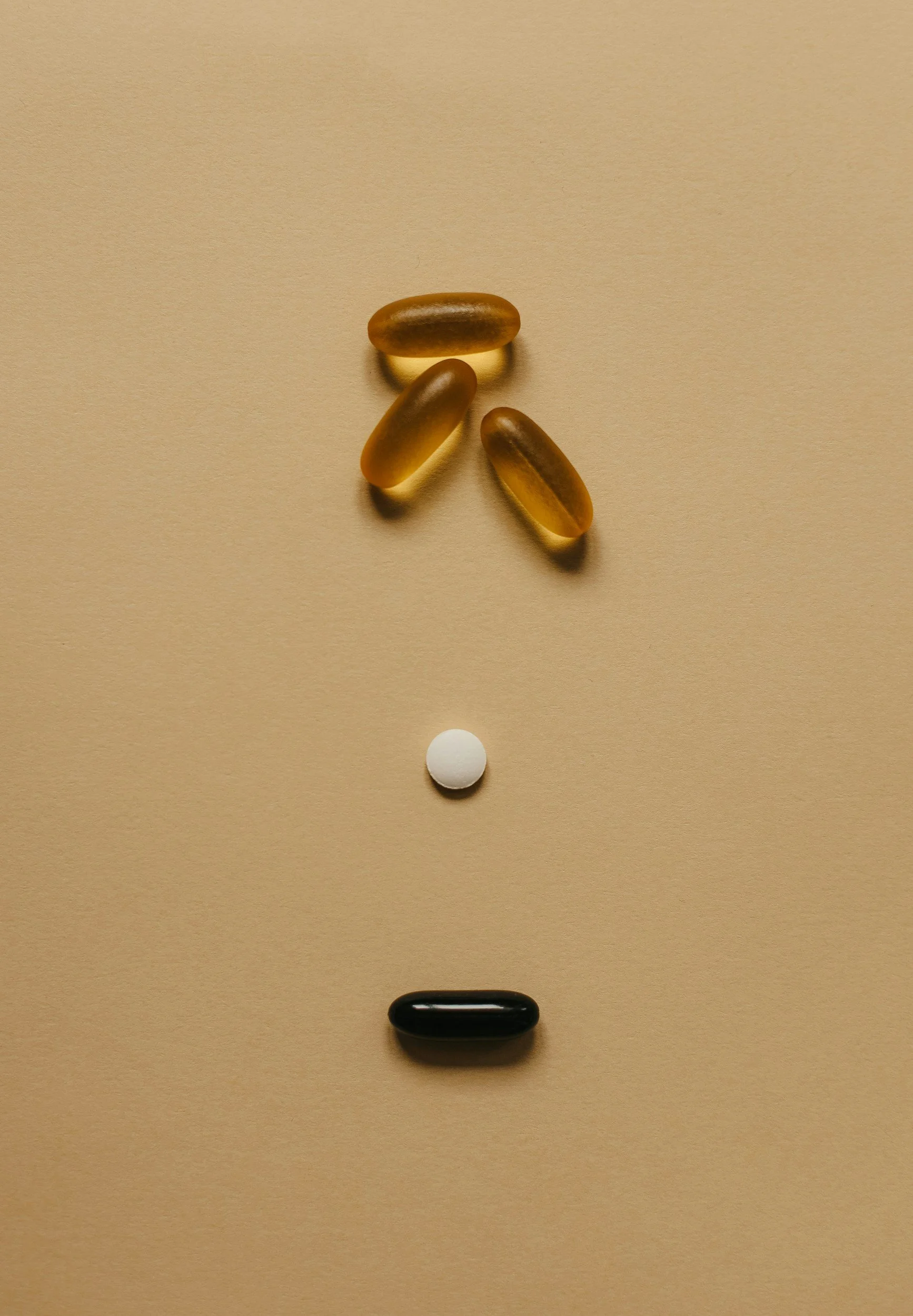 Arrangement of pills and capsules on beige background, mimicking a question mark.