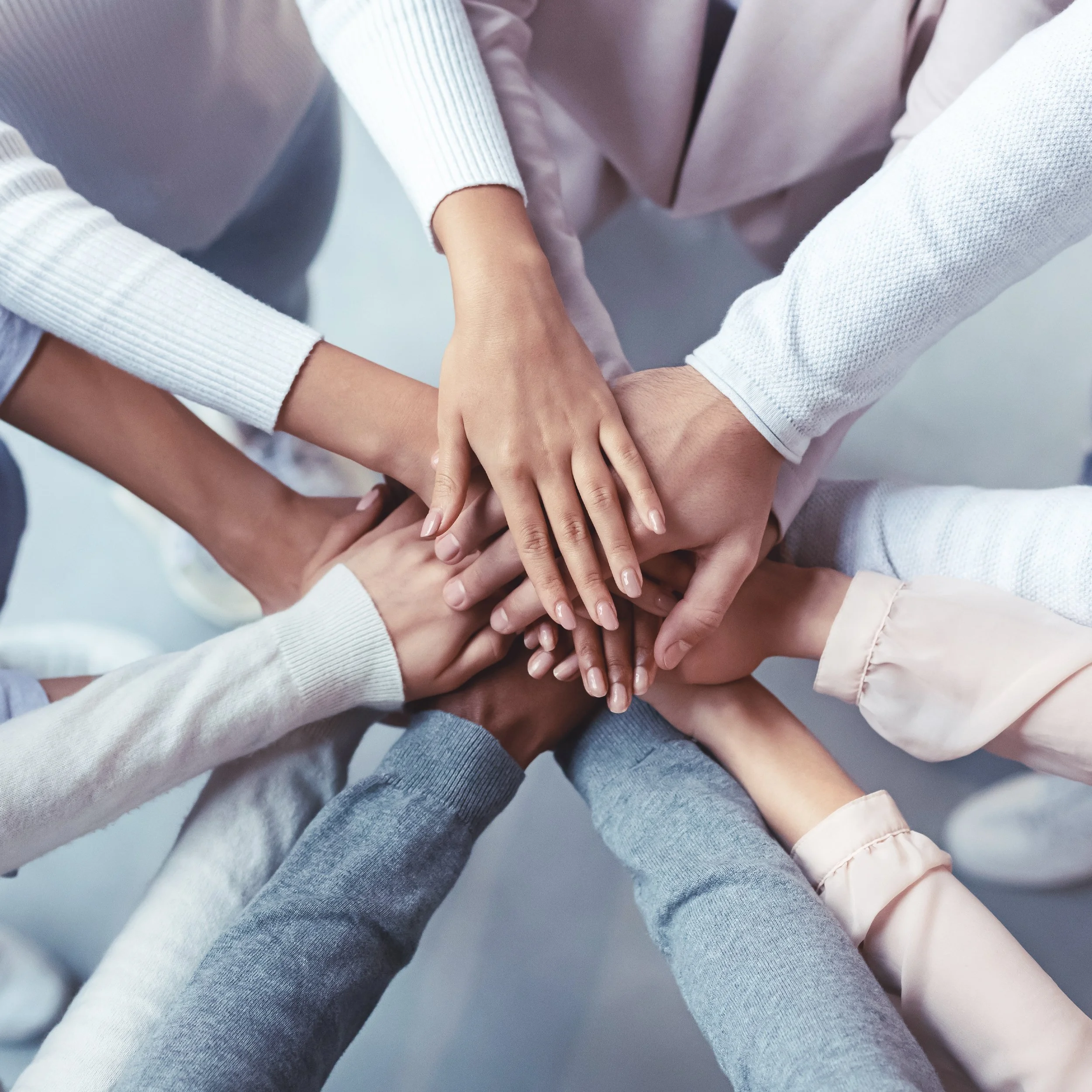 Multiple hands of diverse skin tones stacked together in the center, symbolizing teamwork and unity.