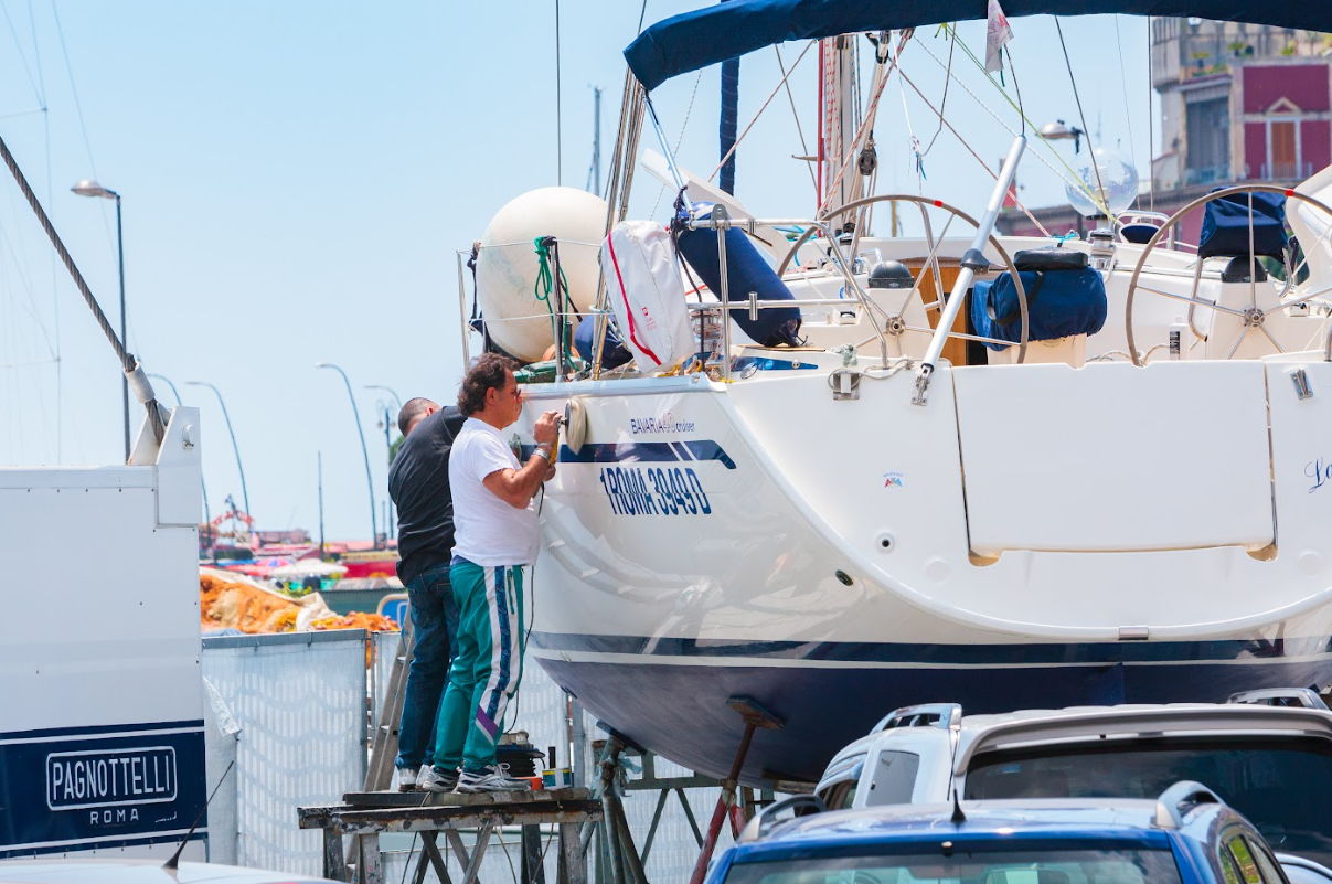 People working on a sailboat in a marina, preparing it for launch.