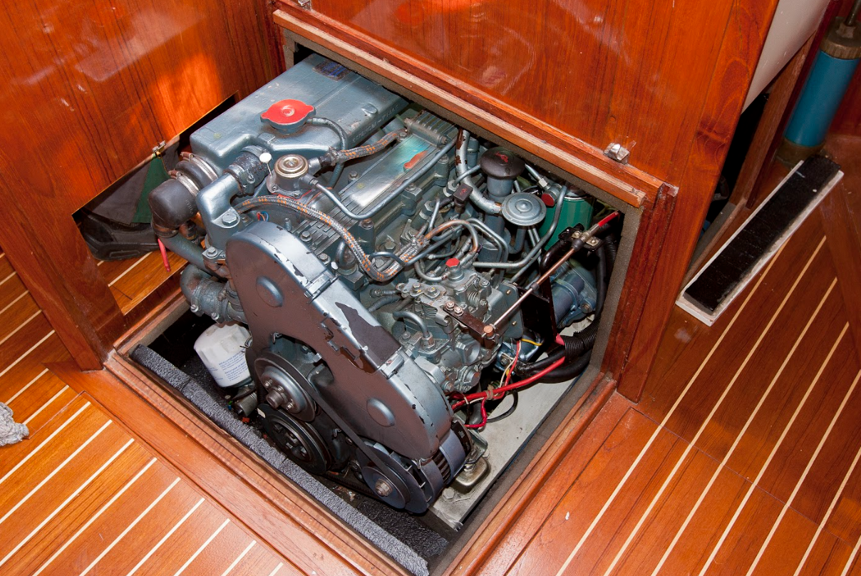 A boat engine inside a wooden compartment with an open lid, showing mechanical parts, hoses, and wiring.