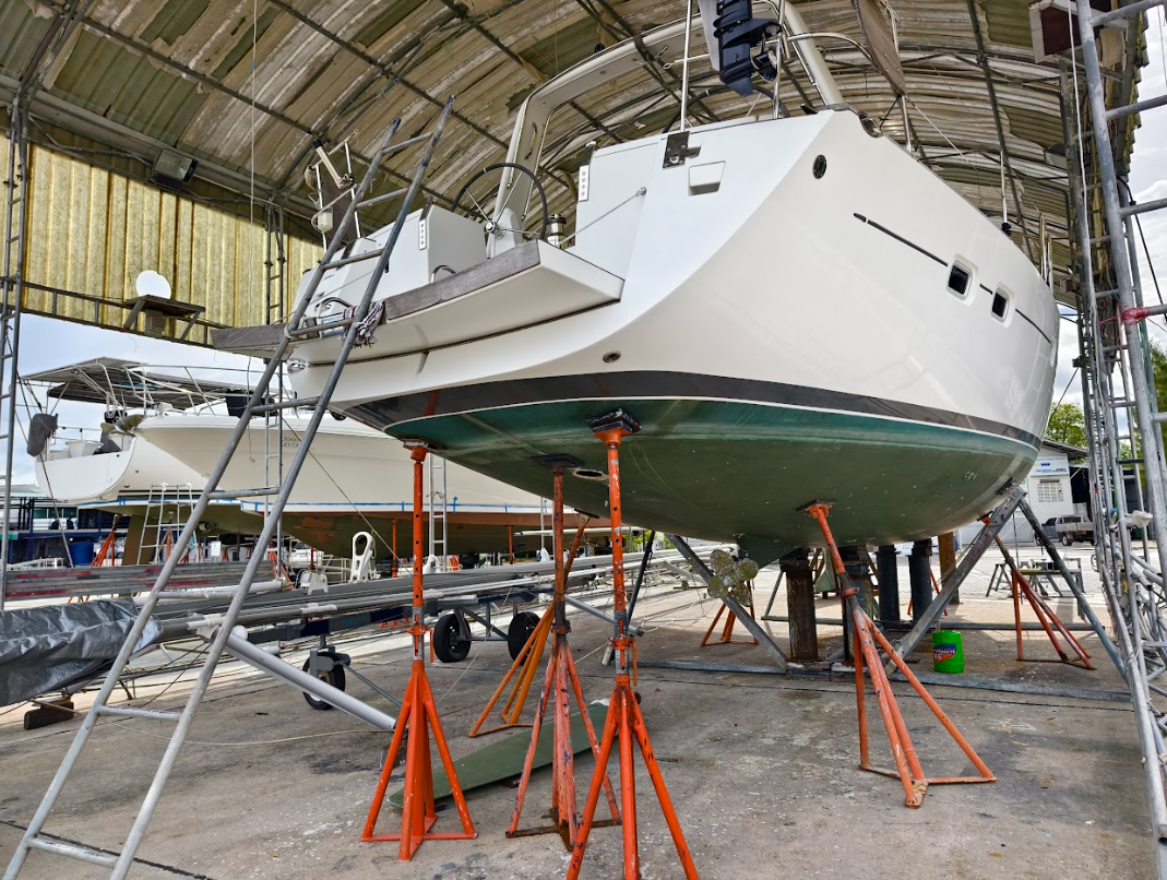 A white sailboat on supports inside a boat storage facility, with scaffolding around it for maintenance or construction.