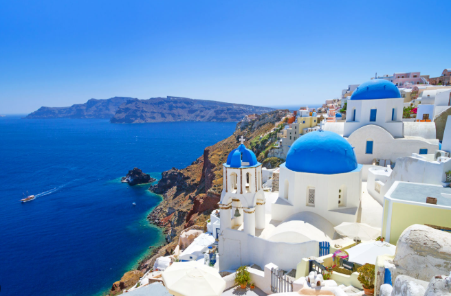 White buildings with blue domes on a hillside overlooking the ocean in Santorini, Greece.