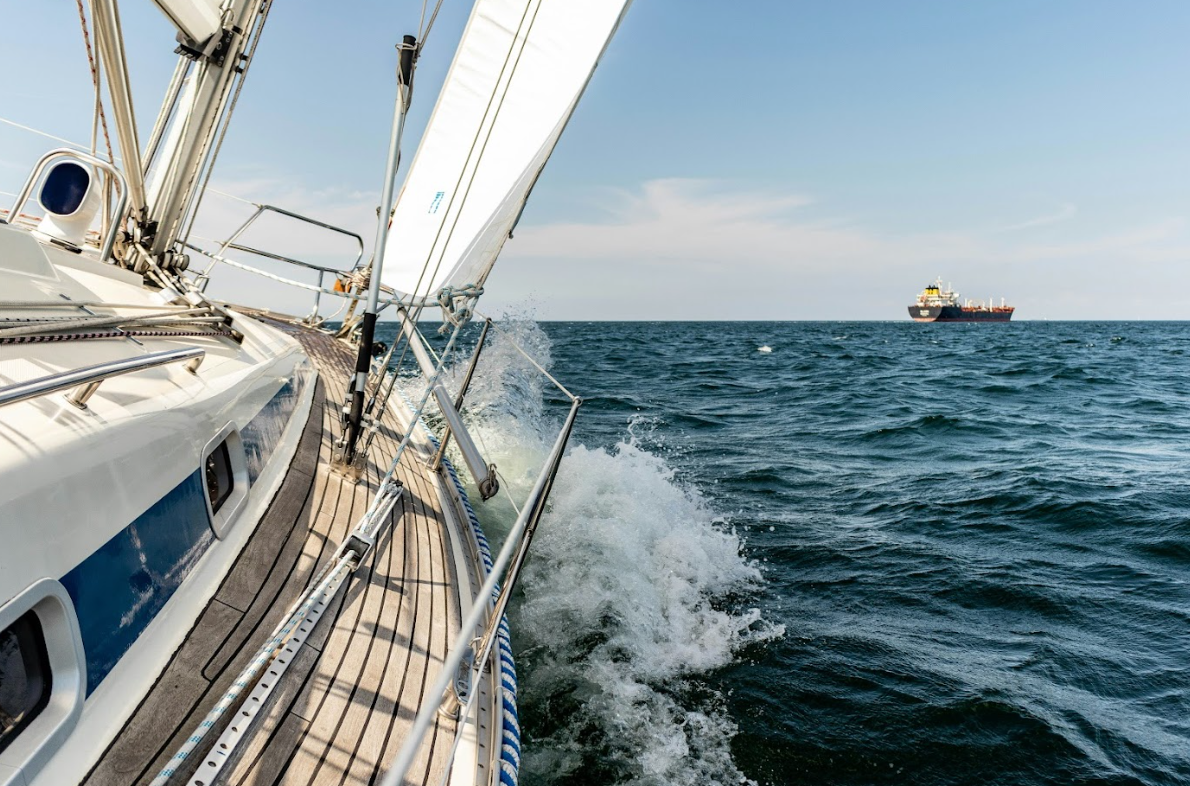 View from a sailboat on the water with a large cargo ship in the distance under a partly cloudy sky.