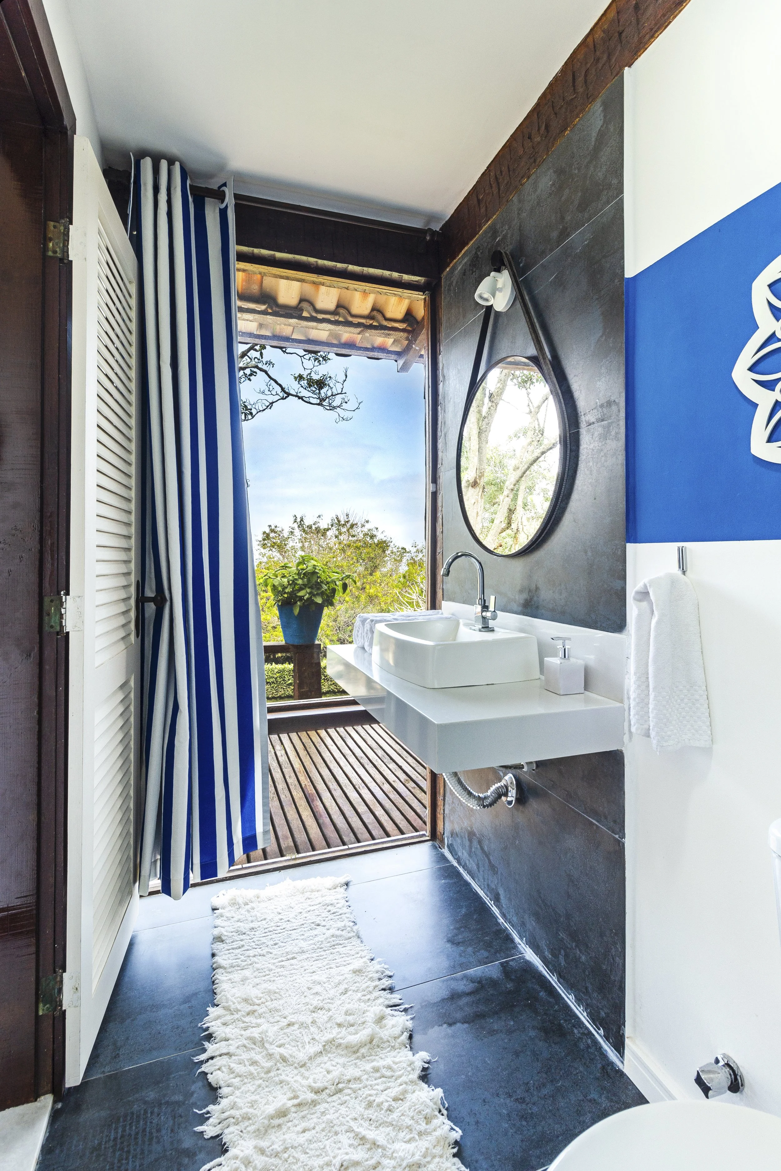Bathroom with a walk-in shower, round mirror, white sink, and a view of trees outside.