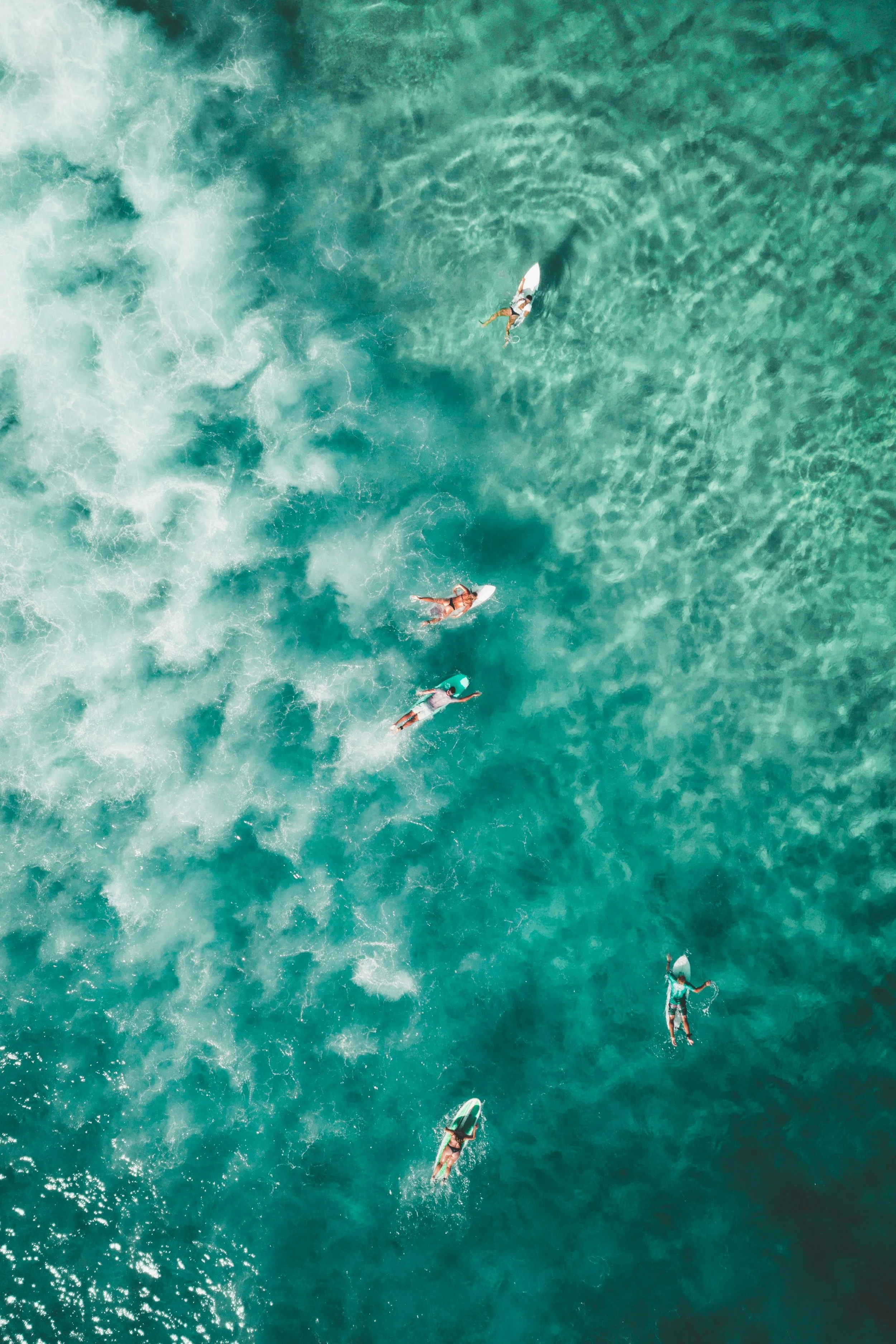 Aerial view of five people surfing on the ocean, wake and waves visible in the water.