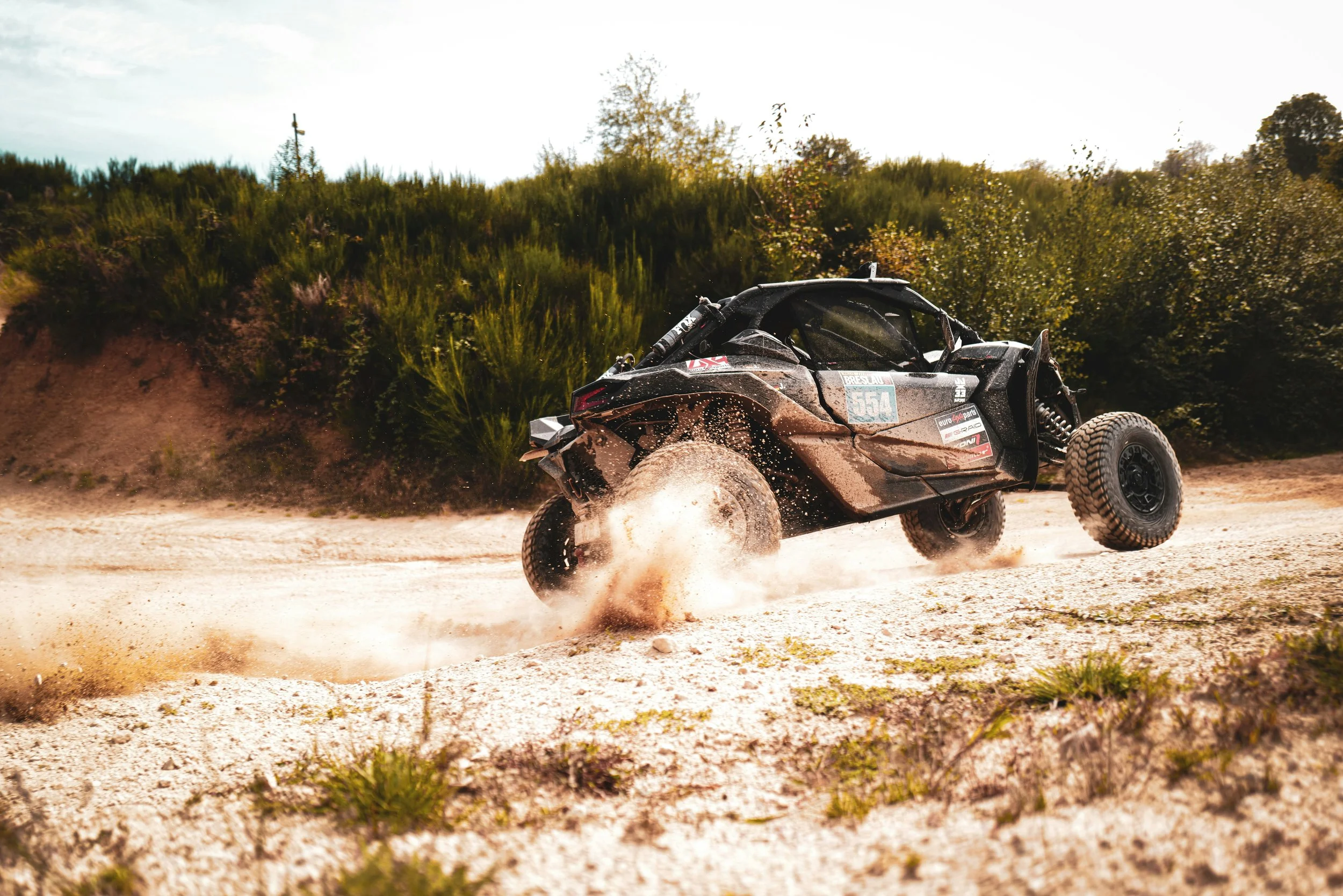 An off-road dune buggy kicking up dirt on a sandy trail in a wilderness area.