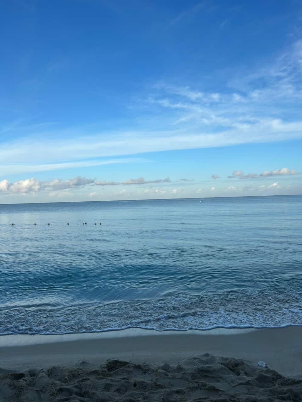 Calm ocean waves at sandy beach with a clear blue sky and some clouds.