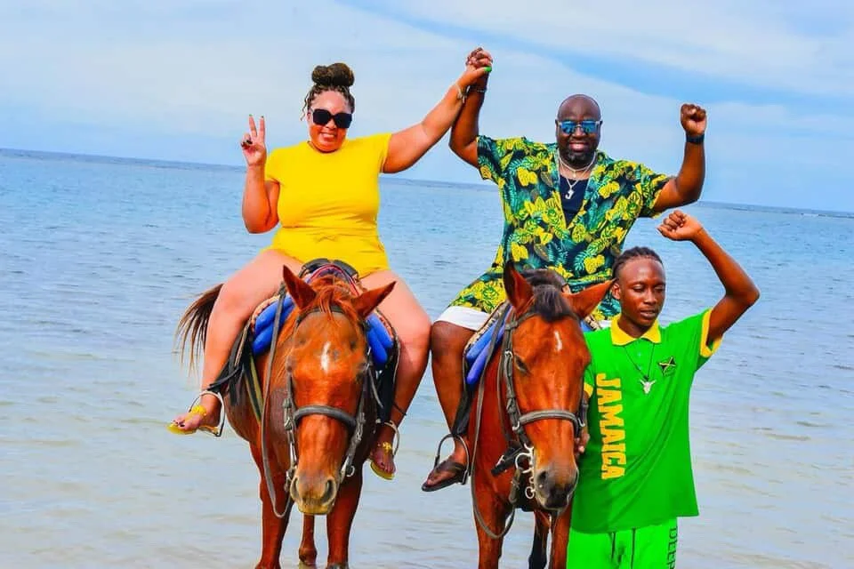 Two people riding horses in the ocean with a woman making peace sign and a man flexing his arm, while a young boy stands with a raised fist.