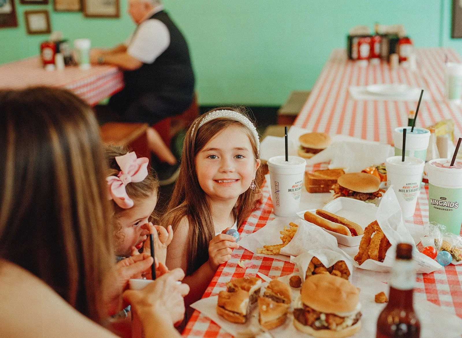 Children smiling at a table with burgers, fries, and drinks.