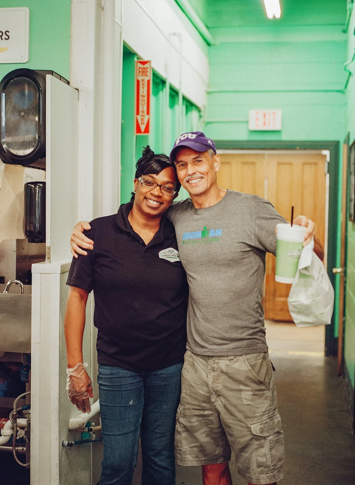 A Kincaid's employee stands arm in arm with a local customer, smiling with a bag of food in hand
