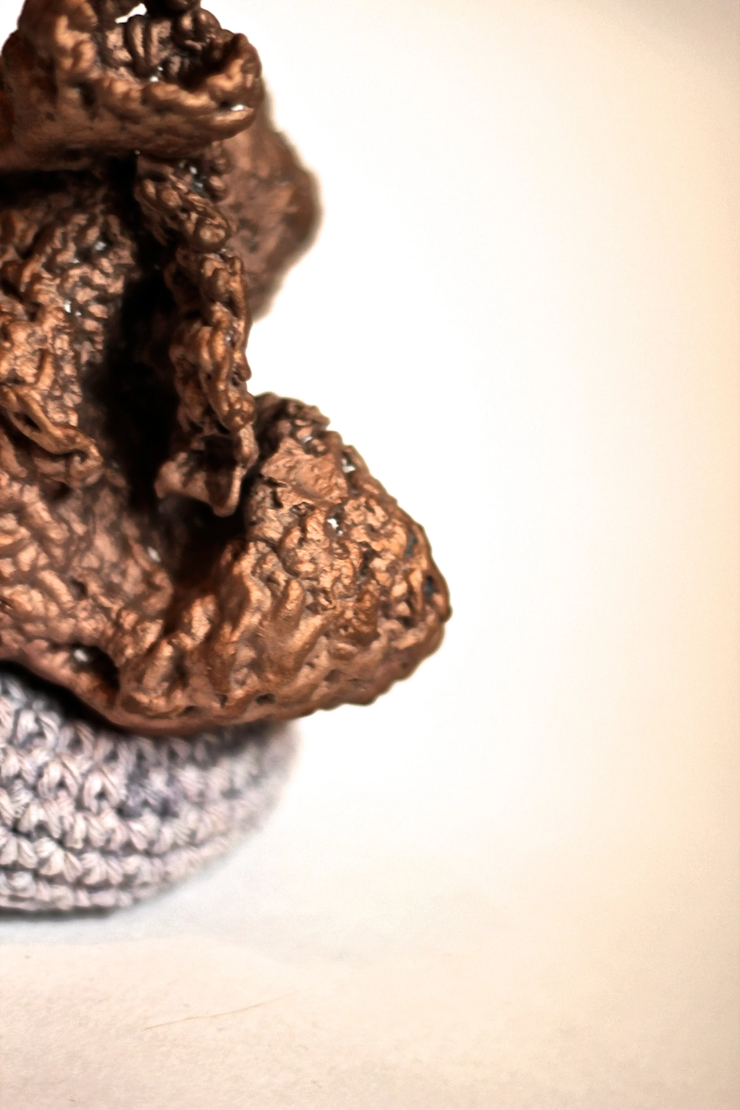 Close-up of a brown, textured pinecone partially covered by a silver, knitted cloth on a white surface.