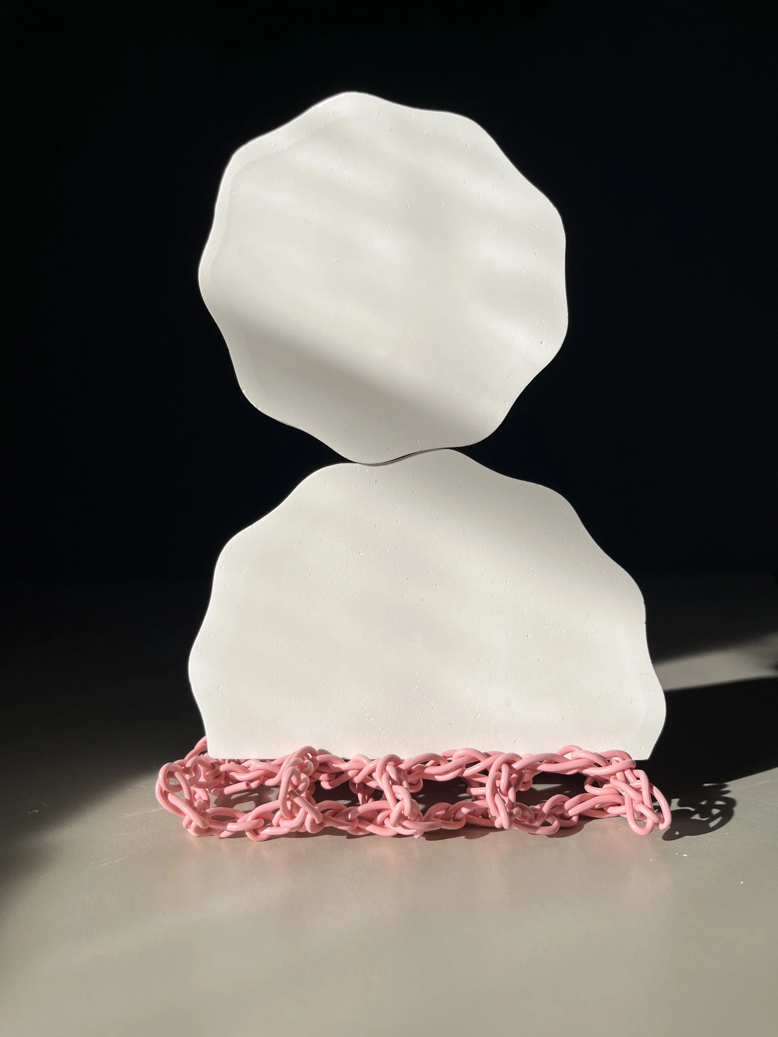 A white, abstract sculpture resembling a human head and shoulders, placed on a pink, chunky chain-link base against a dark background.
