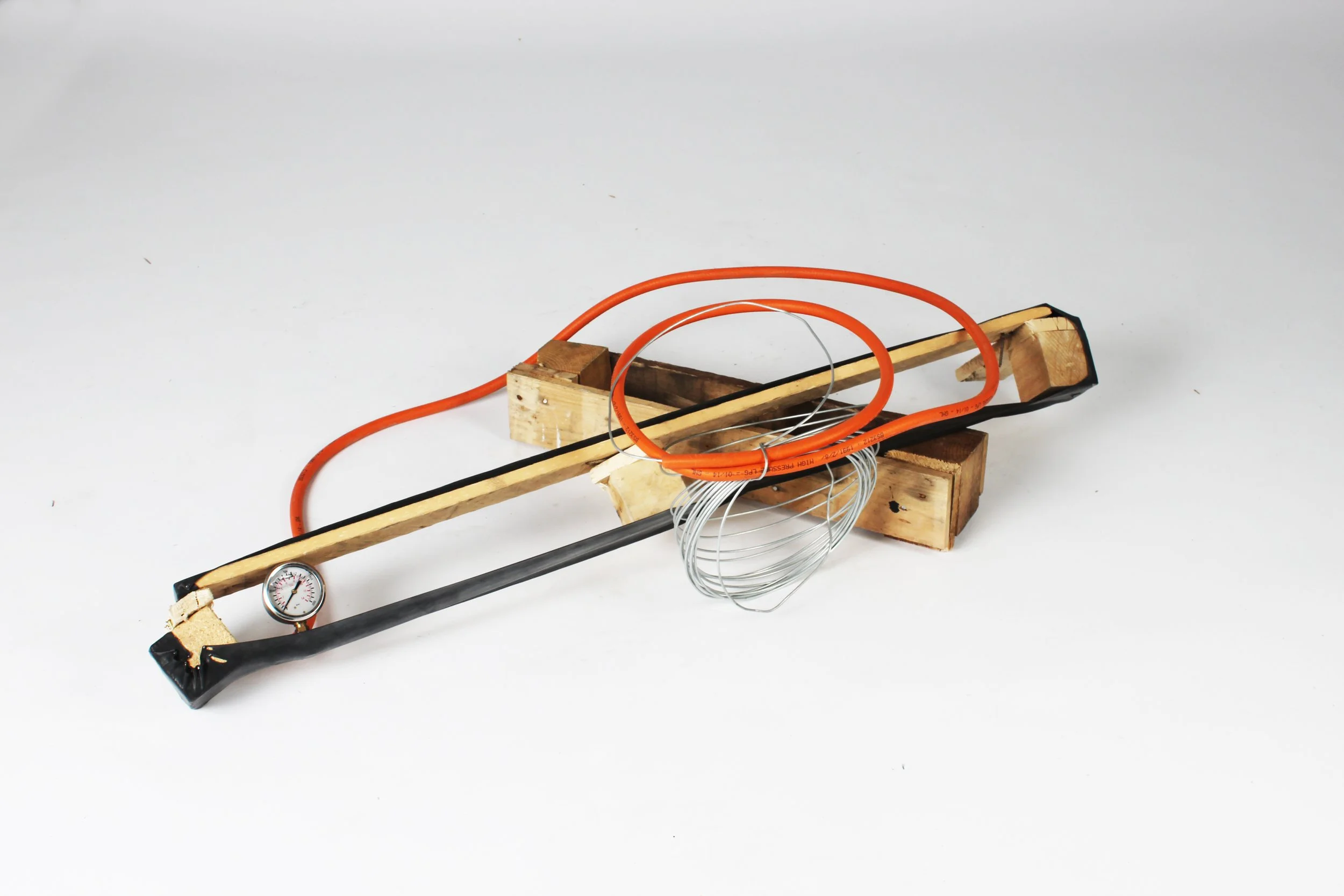 A wooden structure with electrical wires, a gauge, and orange tubing assembled on a white surface.