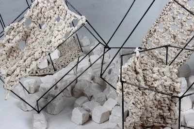 Contemporary art installation with black wireframe structures and white crumpled paper and foam materials.