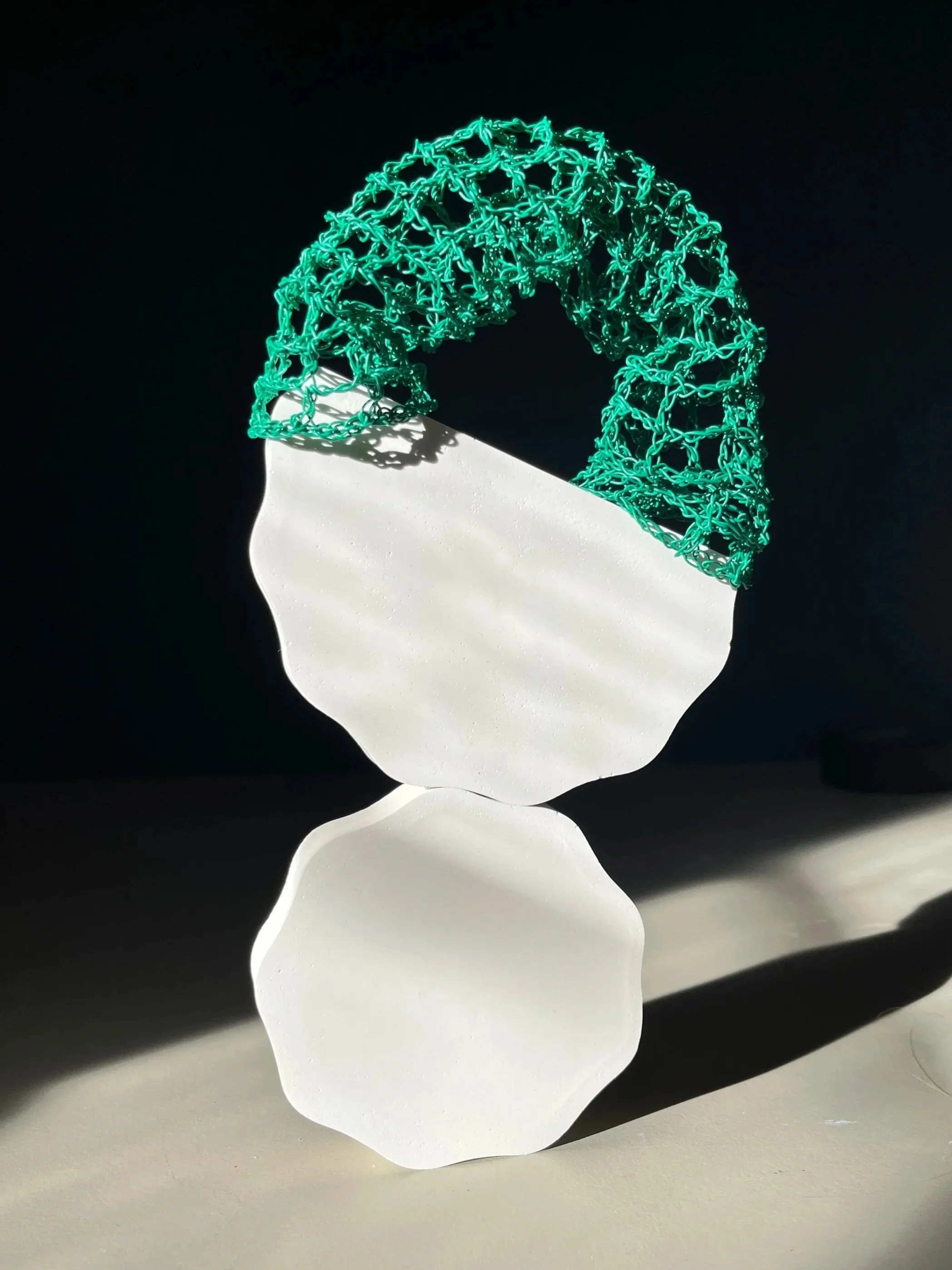 A white sculpture shaped like a human head with a green wireframe top, illuminated against a dark background.