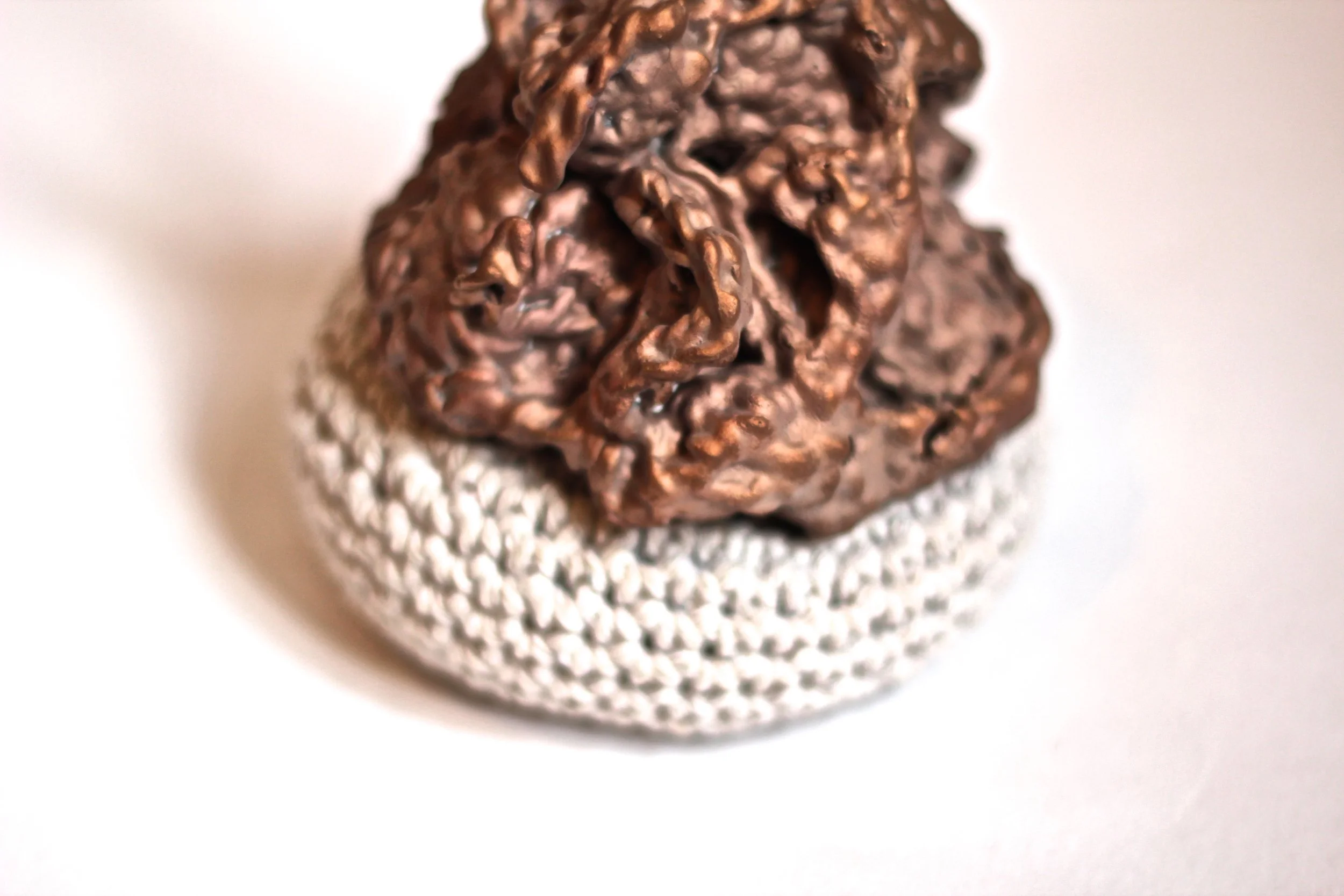 Close-up of a metallic, textured object resembling a crumpled or wrinkled sphere, placed on a white surface with a plain background.