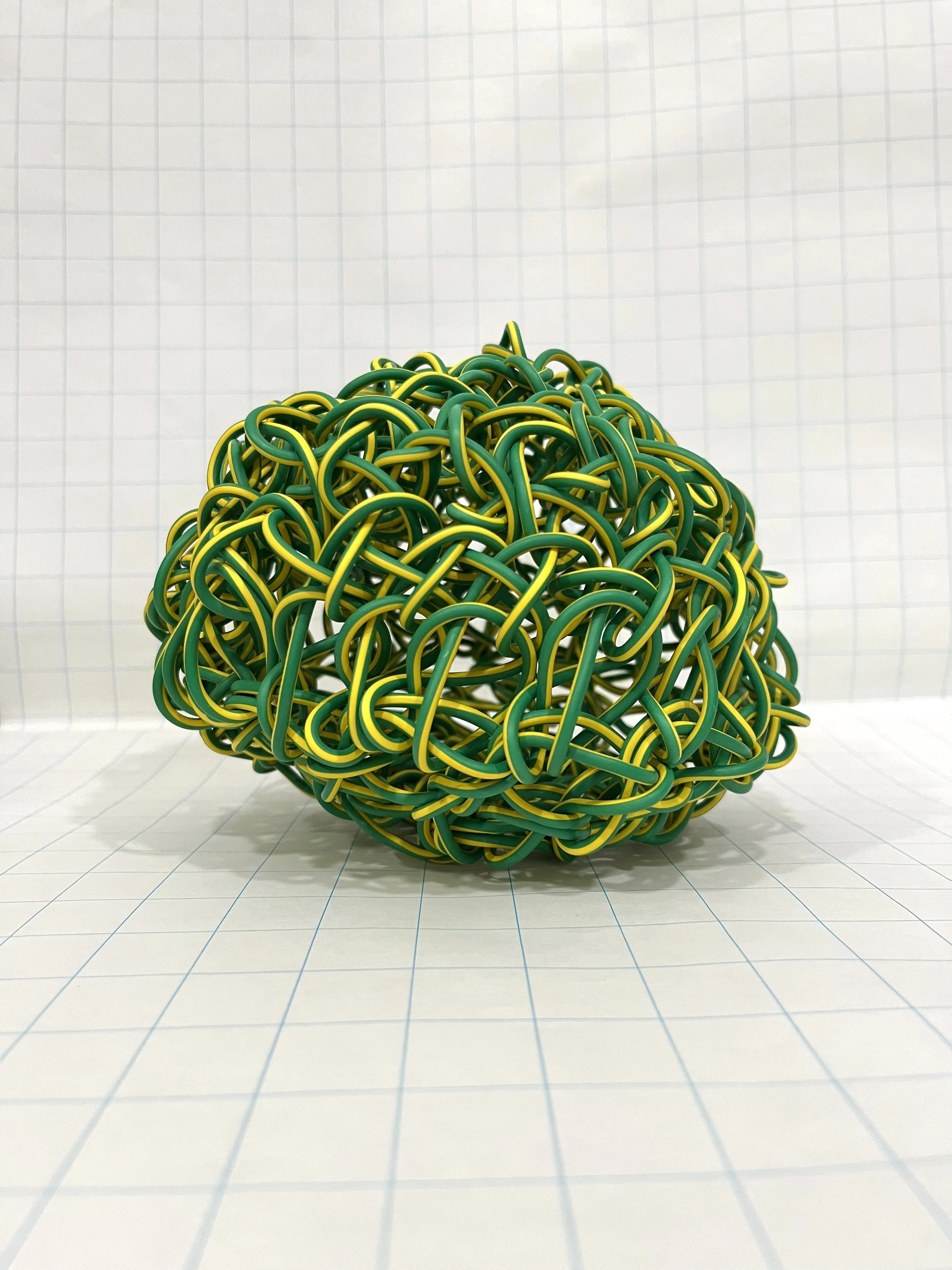 A large ball of intertwined green and yellow rubber bands on grid paper background.