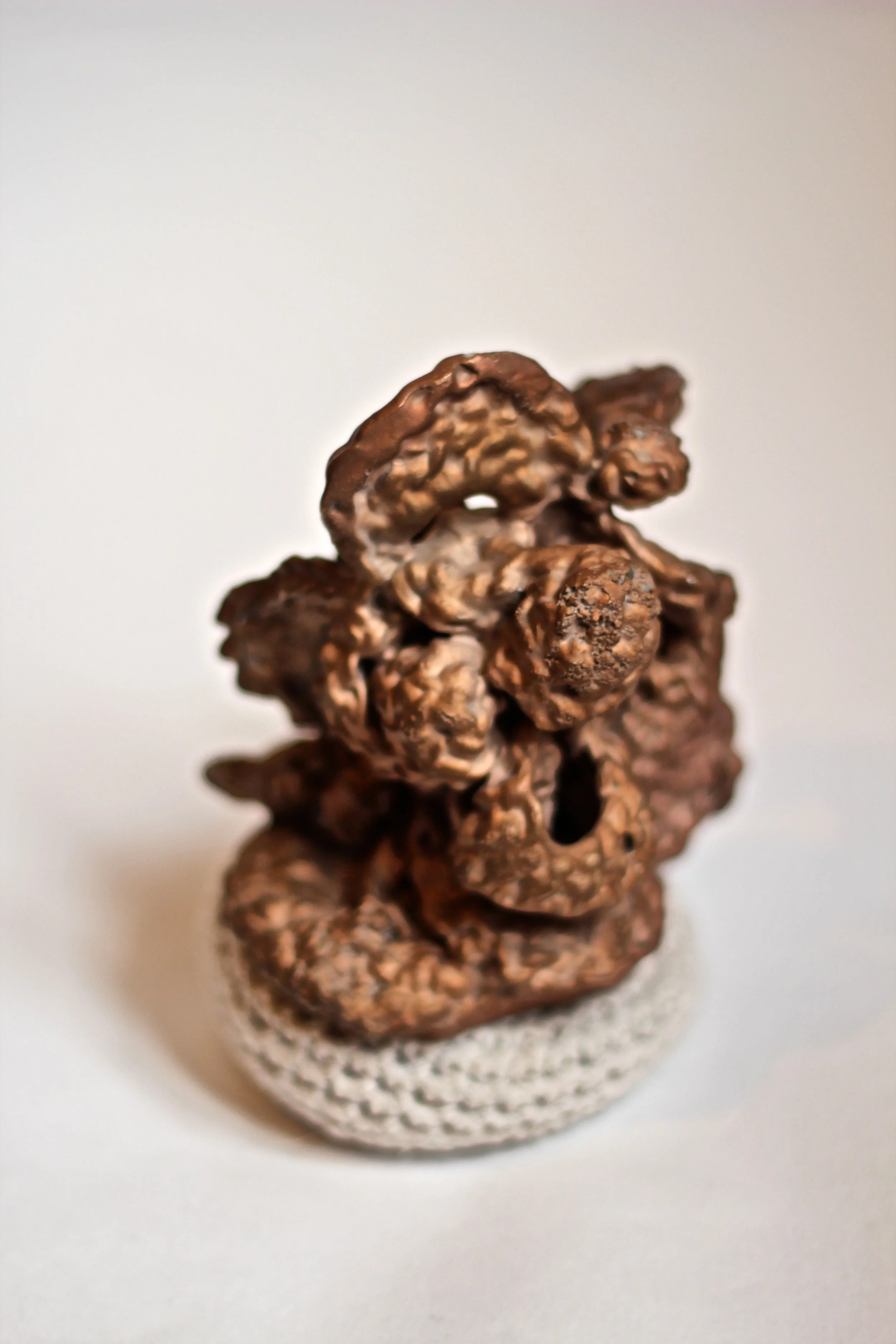 Close-up of a small, textured, brownish ornament with multiple knobby protrusions, placed on a white, textured surface.