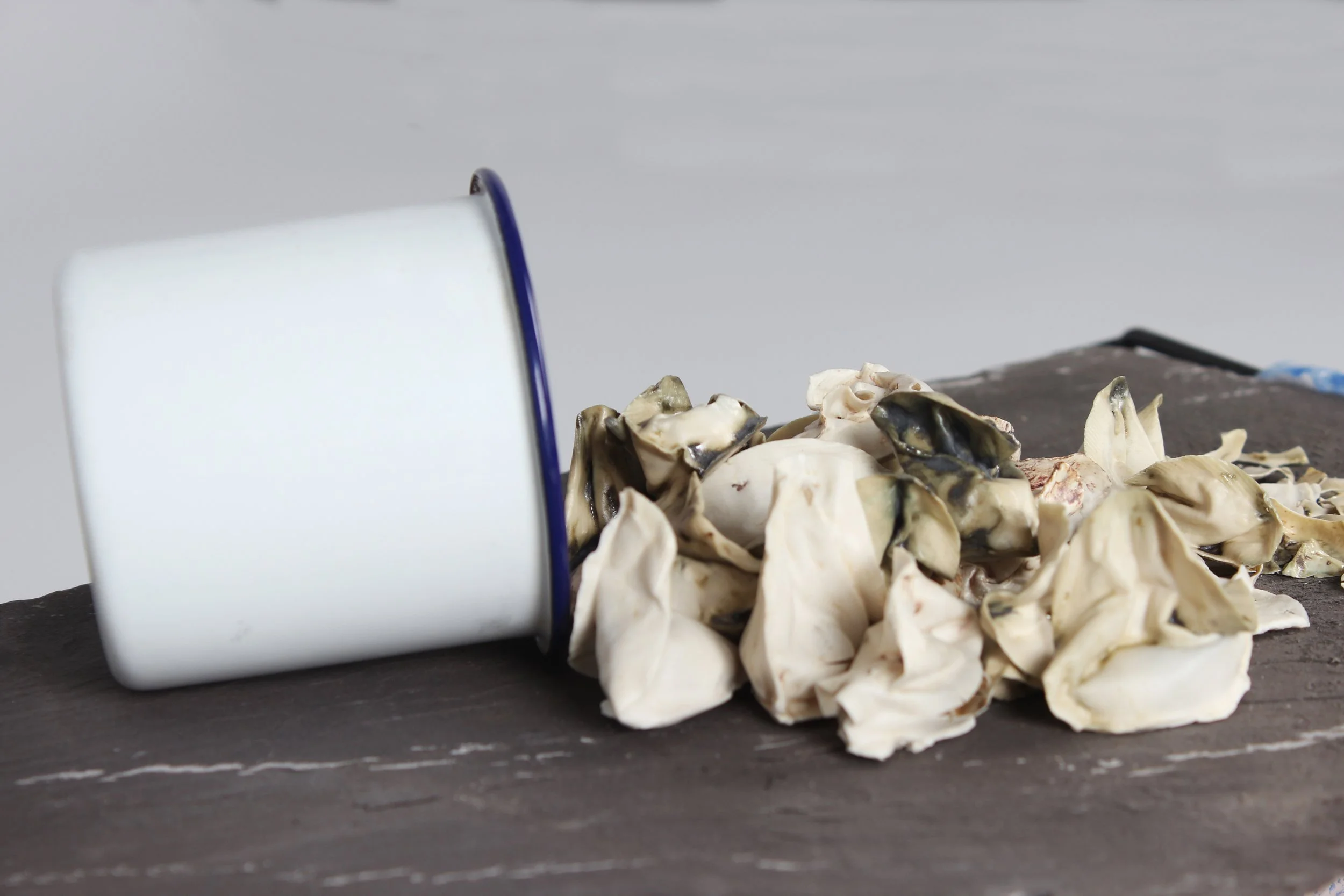 A pile of chopped raw oysters on a dark surface with a white container partially visible to the left. The background is plain and light-colored.