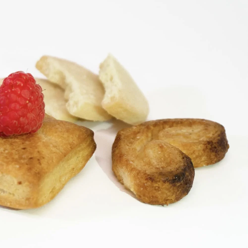 Two cooked chicken drumsticks, a raspberry, and a piece of cheese on a white background.